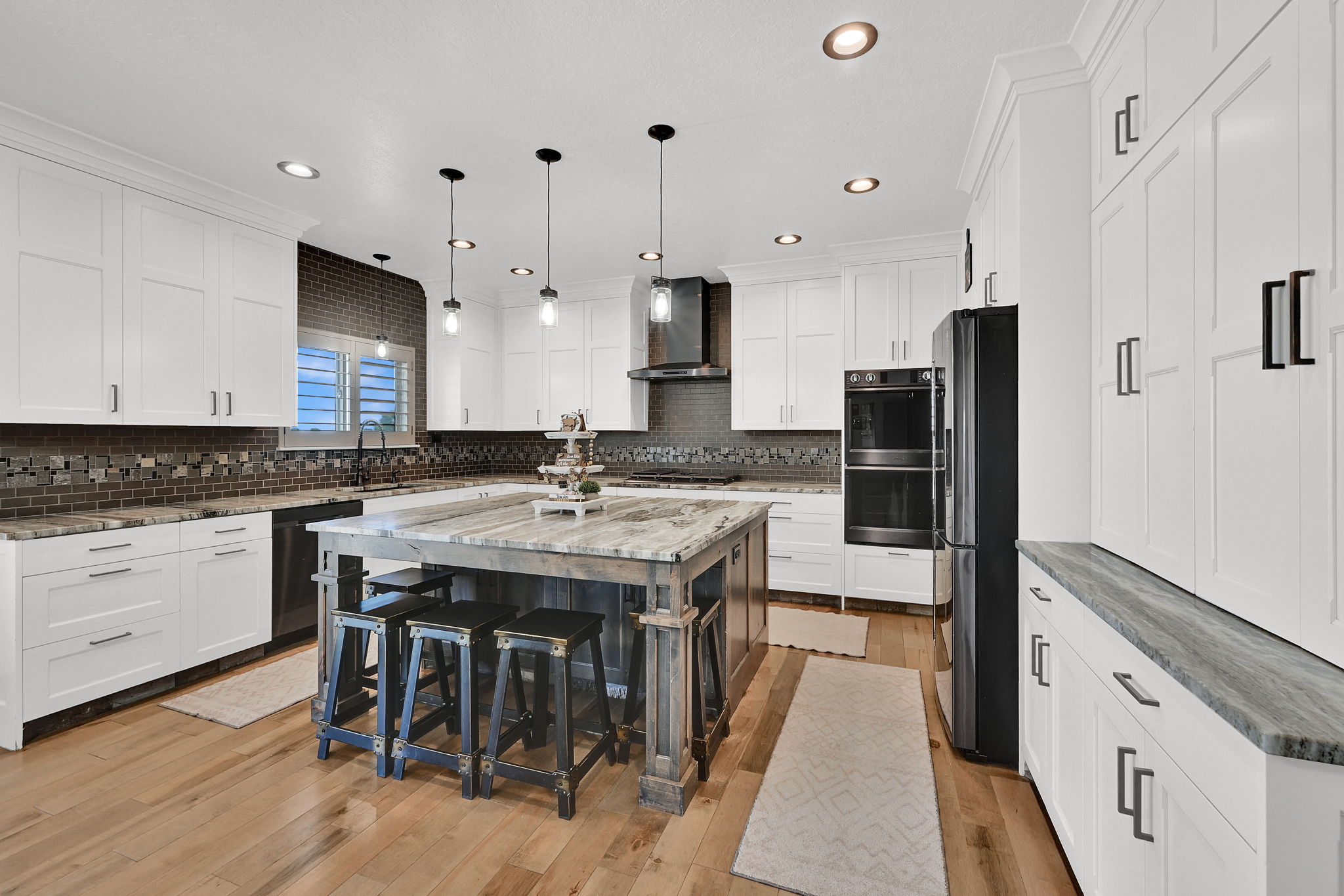 Modern kitchen featuring a large central island with seating, white shaker-style cabinetry, stainless steel appliances, and wood-finish flooring