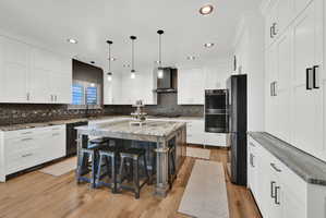 Modern kitchen featuring a large central island with seating, white shaker-style cabinetry, stainless steel appliances, and wood-finish flooring