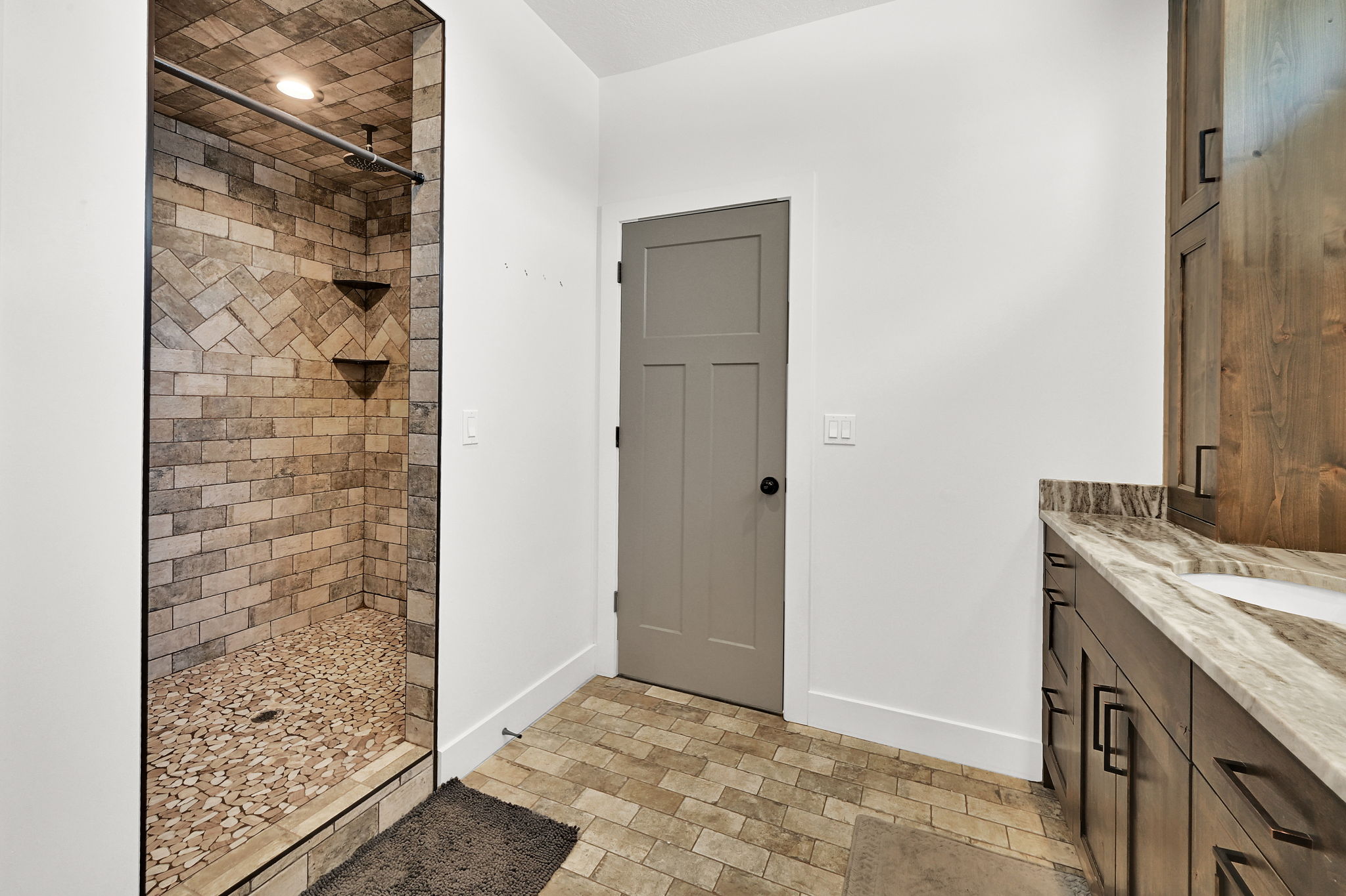 Walk-in shower featuring herringbone-patterned tile walls and a river rock floor