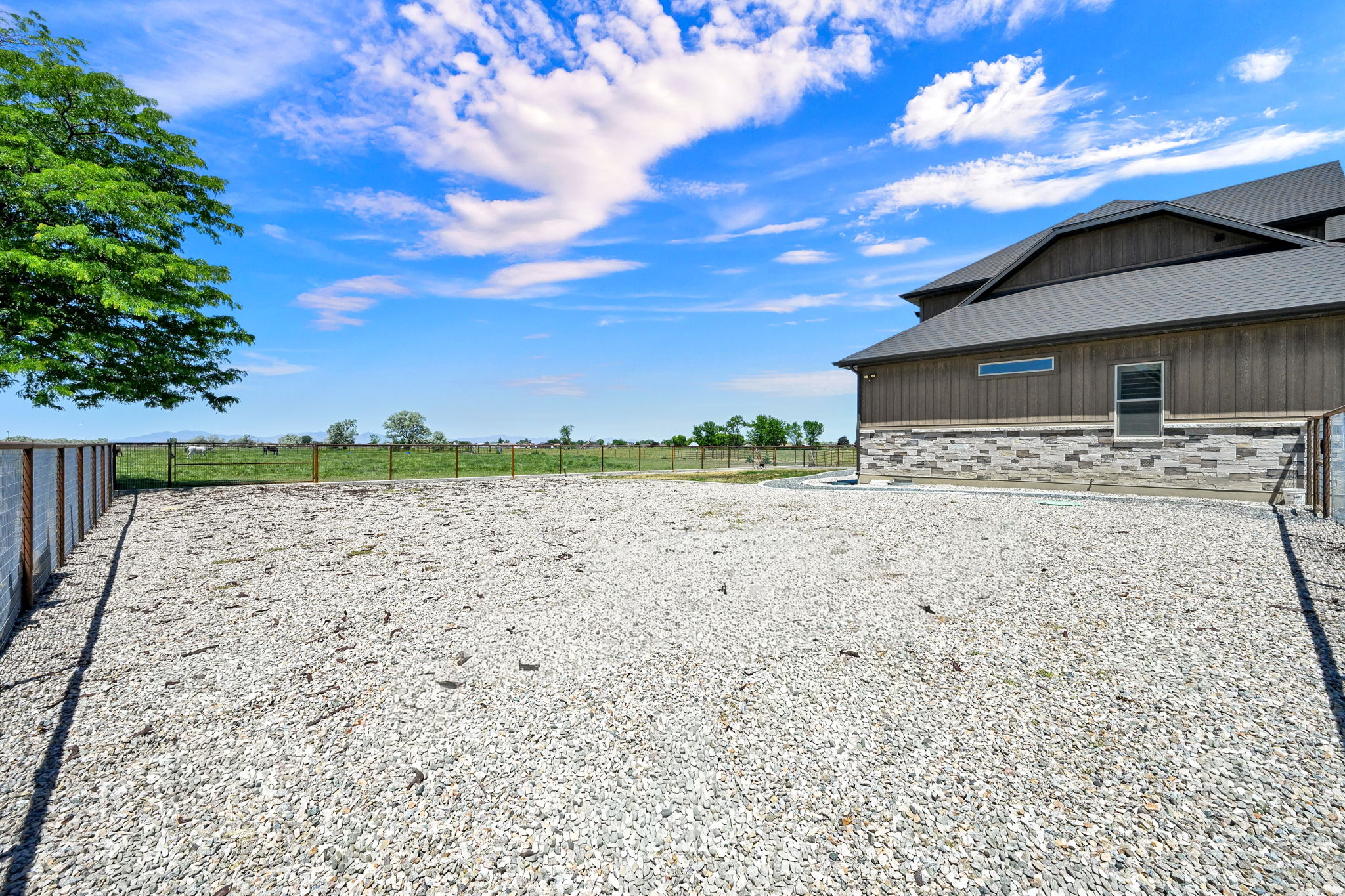 Expansive gravel outdoor area featuring a modern two-story exterior with vertical siding and a stone accent facade