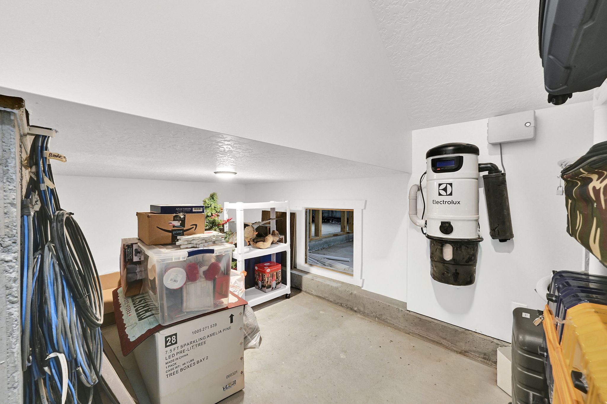 Utility space featuring a wall-mounted central vacuum system, concrete flooring, and a low-set window with white trim