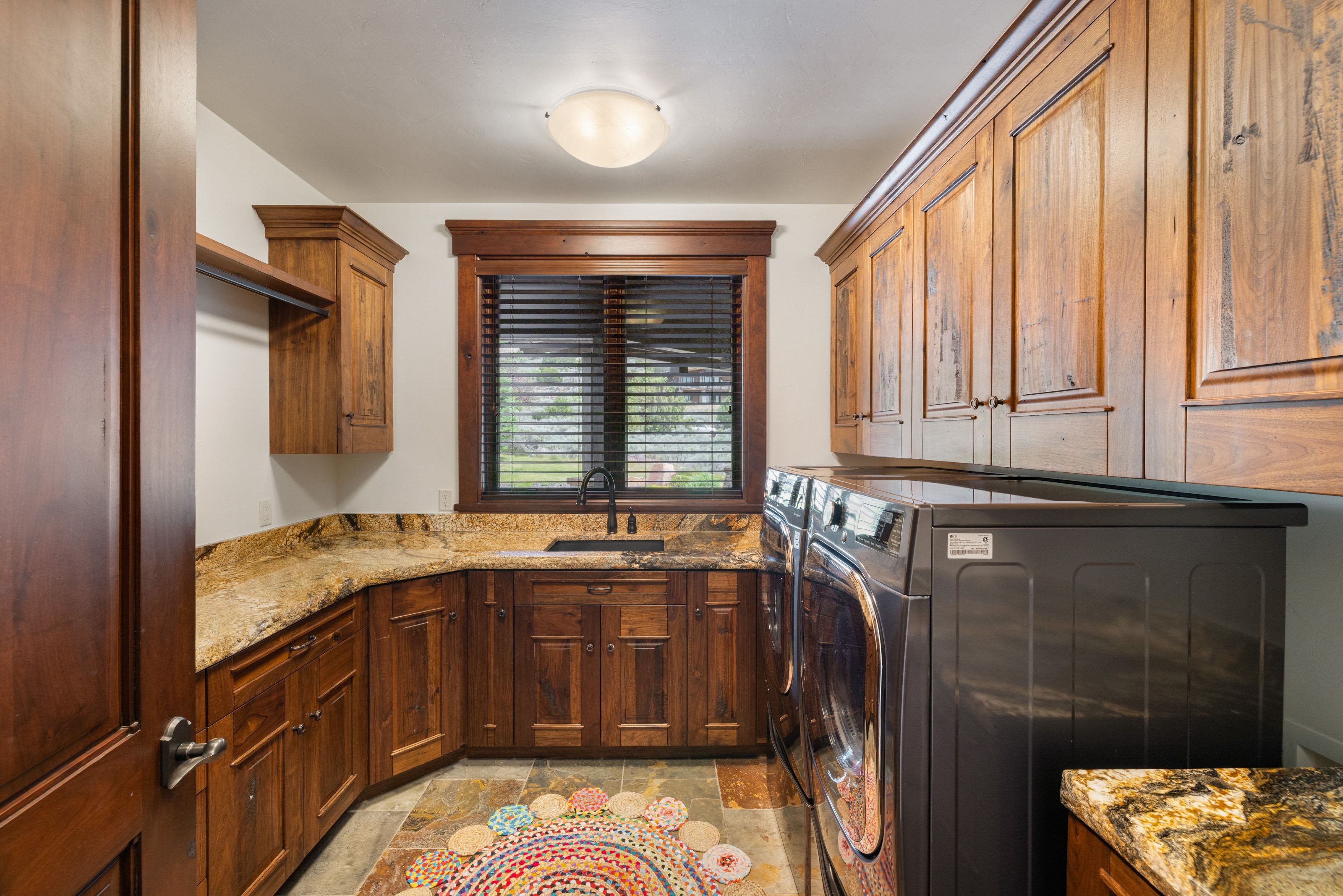 Utility room featuring extensive wood cabinetry, stone countertops, integrated sink with a black faucet, and patterned floor tile
