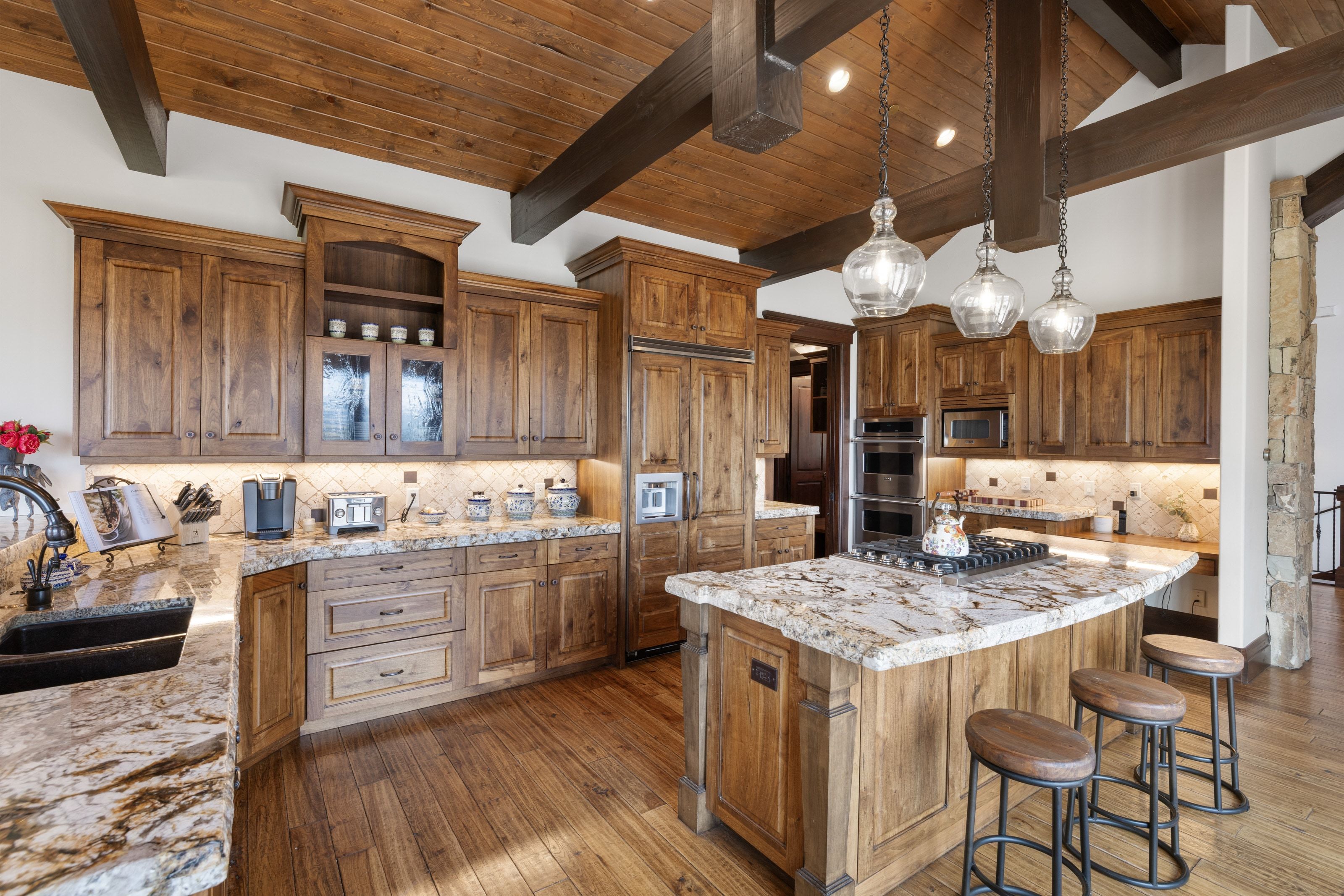 Gourmet kitchen with wood-finish flooring, custom wood cabinetry, and a stone-clad island with a cooktop