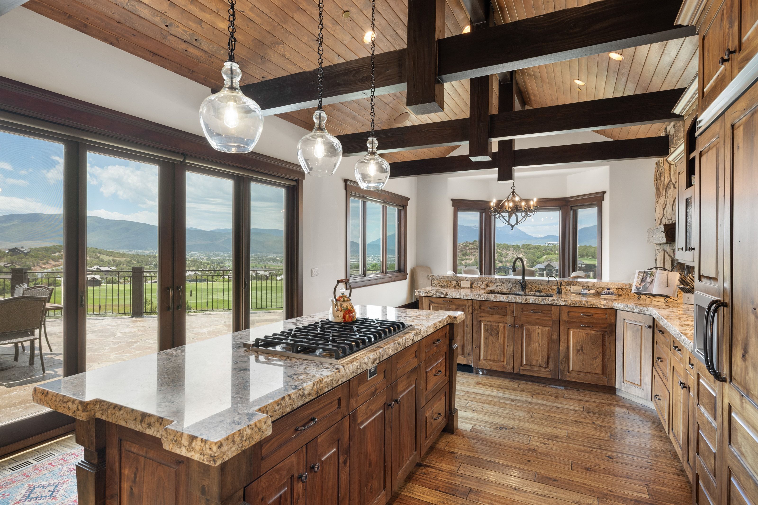 Kitchen featuring a gas range on a stone-topped island, wood-finish flooring, exposed wood beams, and extensive wood cabinetry