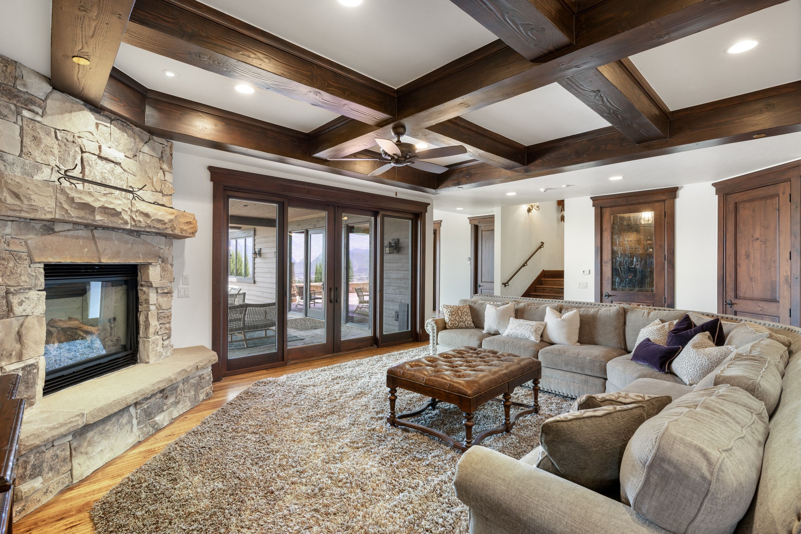 Spacious living area featuring a floor-to-ceiling stone fireplace, exposed wood ceiling beams, and polished wood-finish flooring