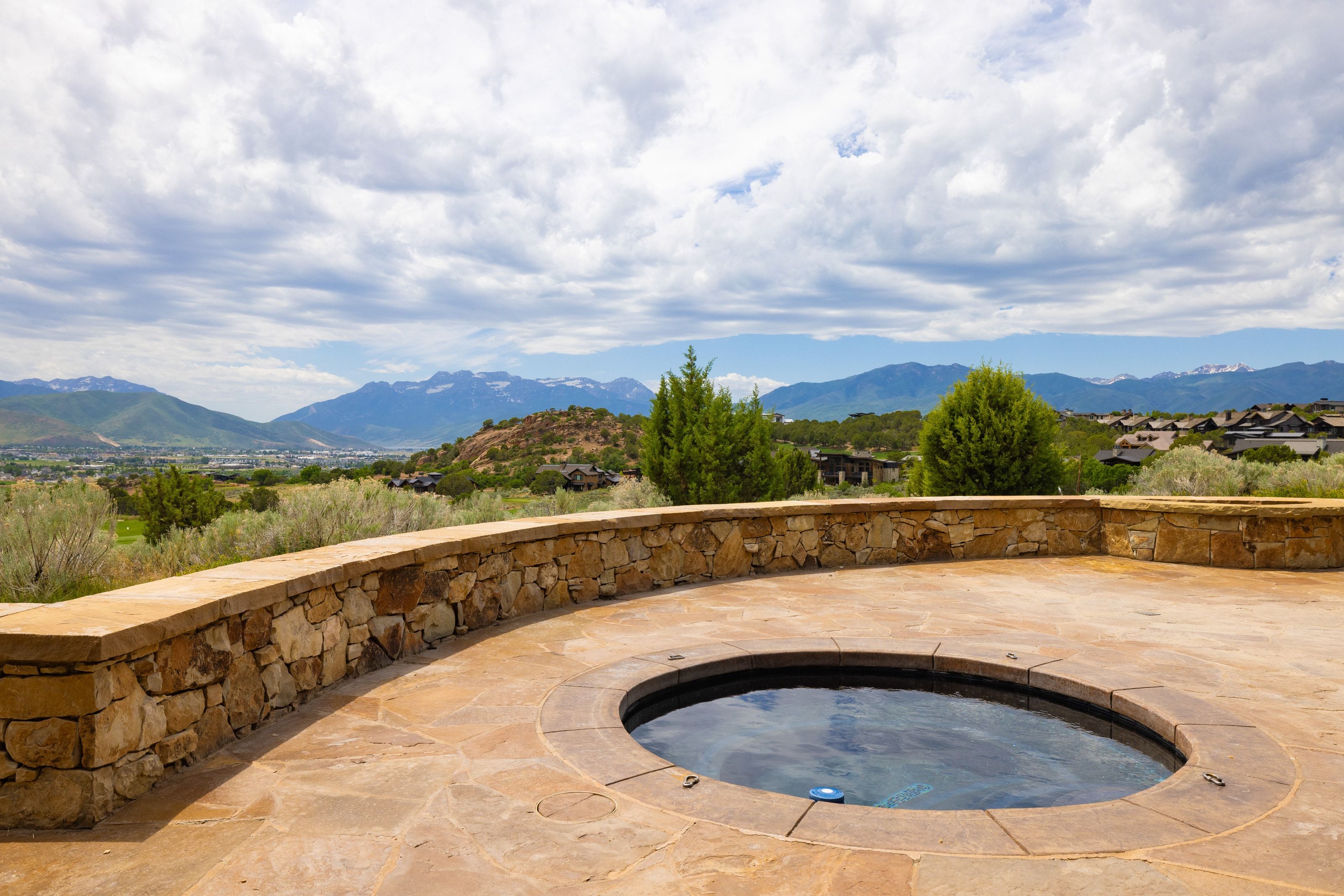 Stone patio with built-in spa, curved stone retaining wall, and distant mountain scenery