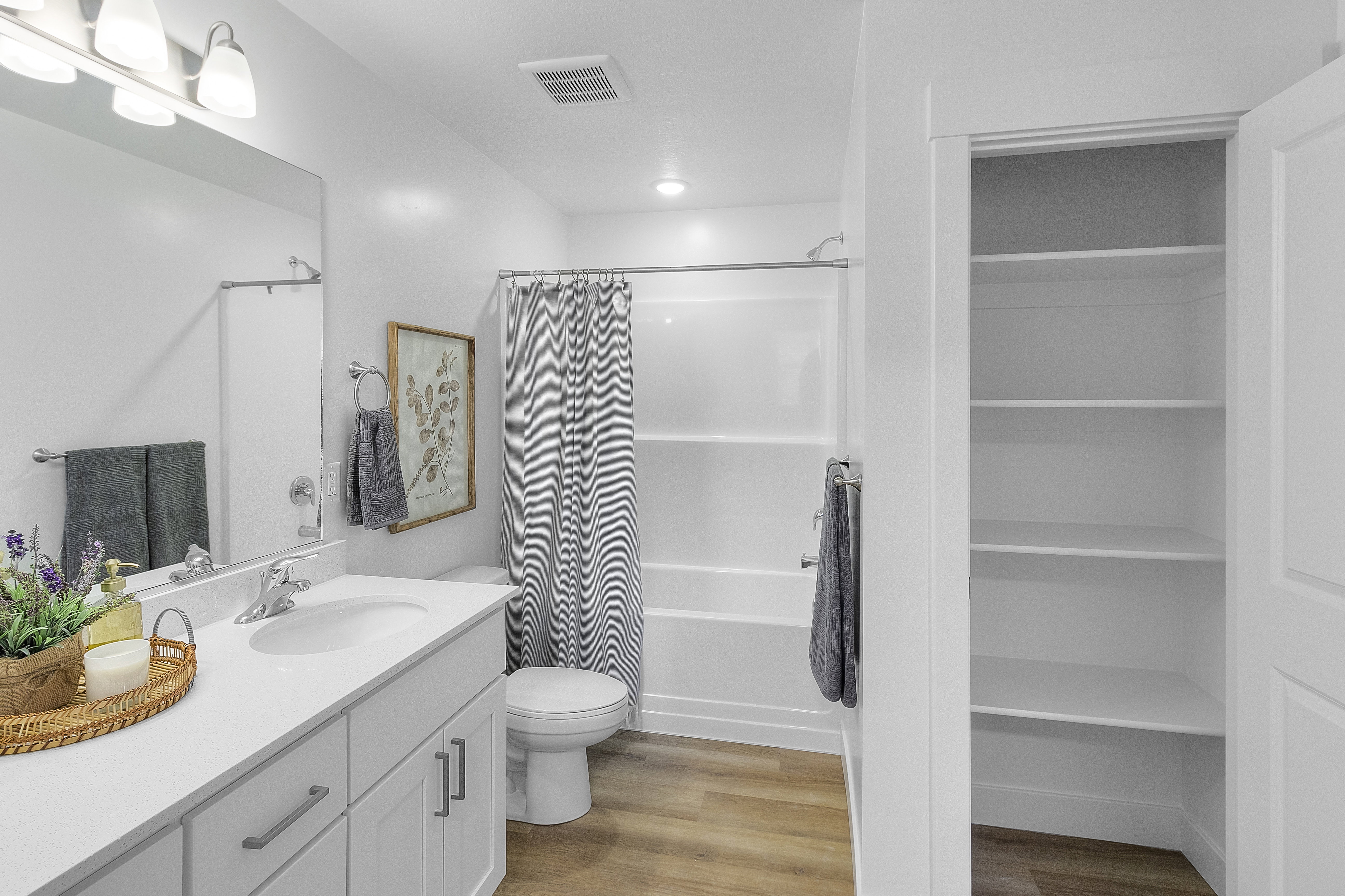 Bathroom featuring a white vanity with integrated sink, white tub/shower combination, and wood-finish flooring