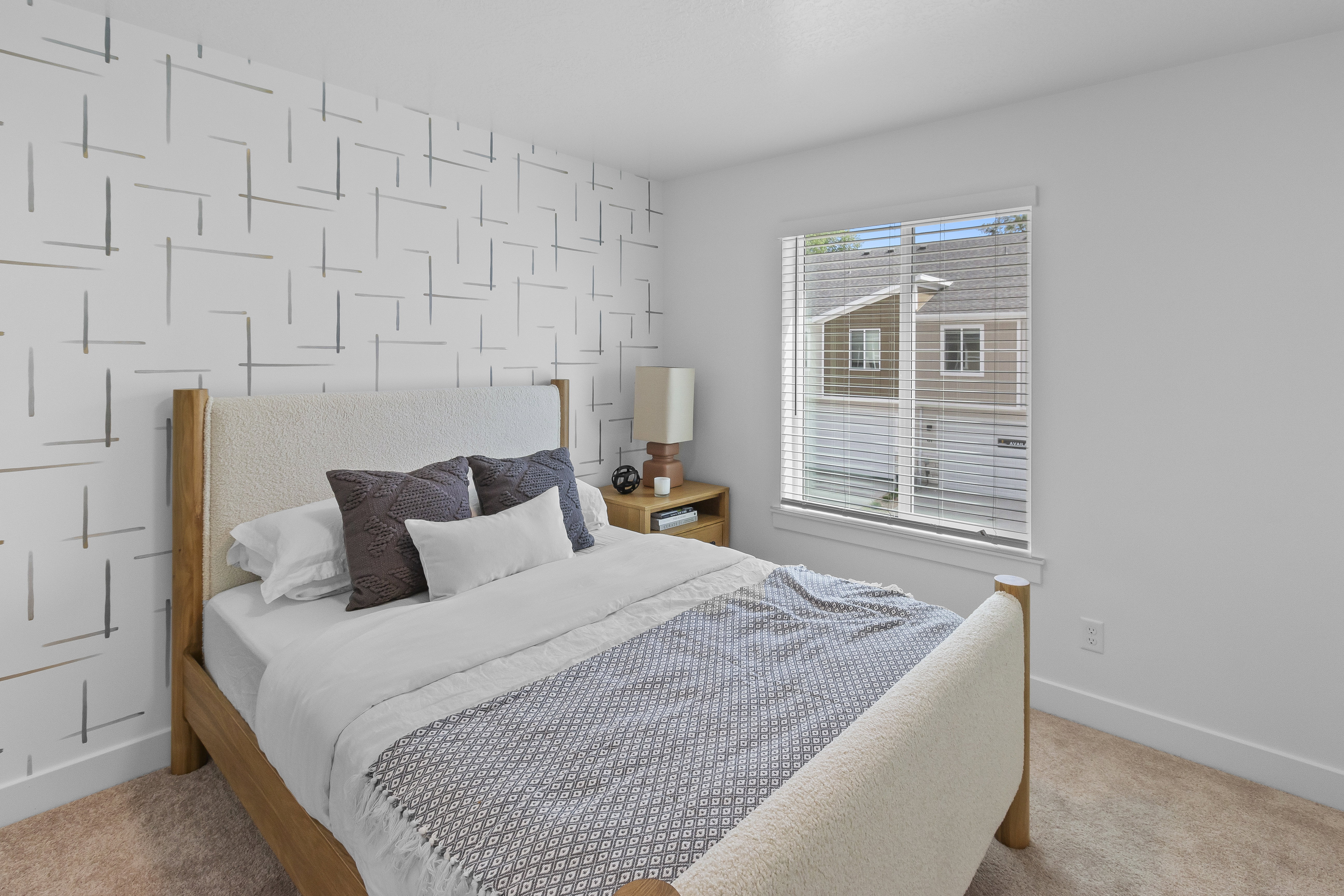 Bedroom featuring patterned accent wall, neutral carpeting, and a window with blinds