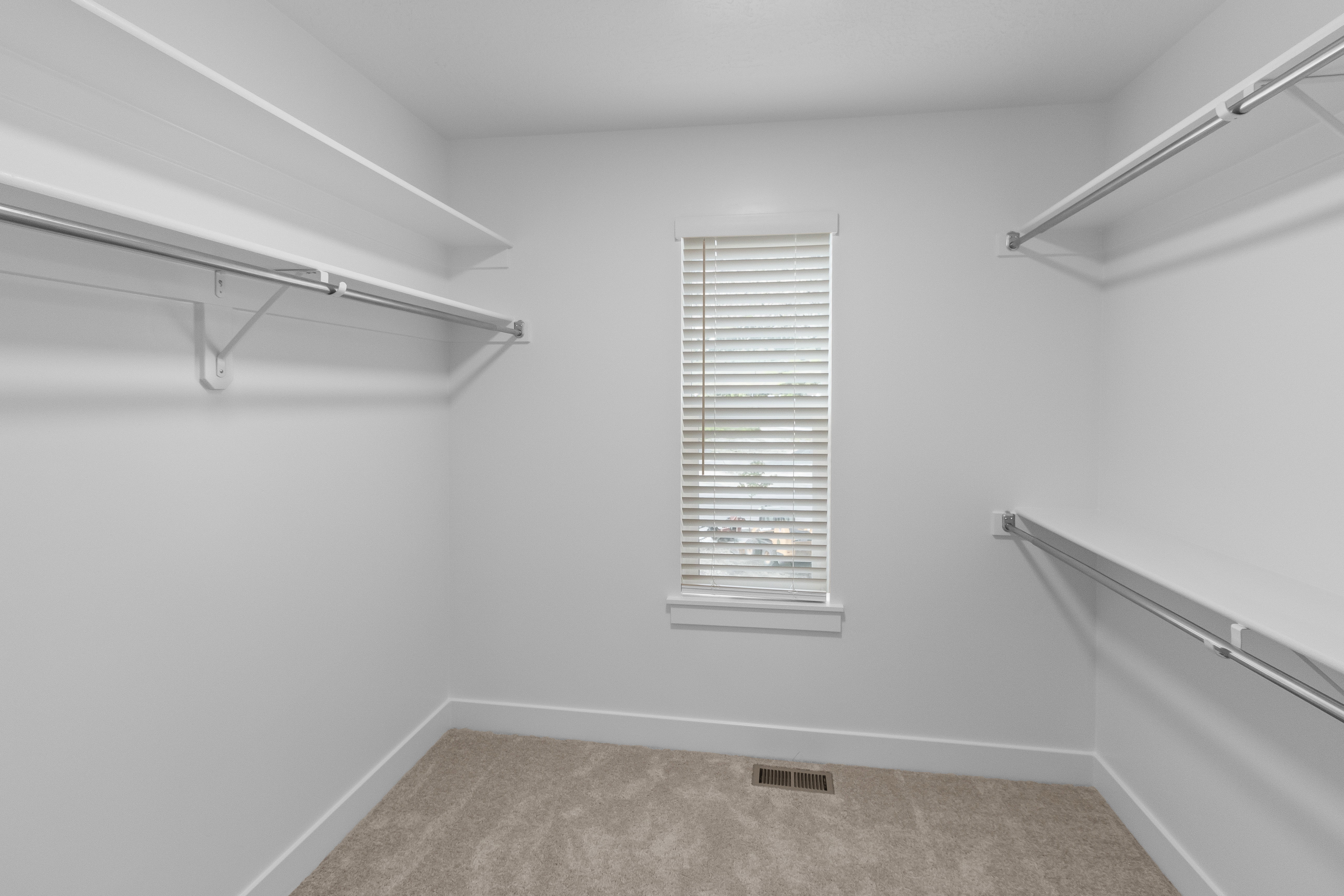Walk-in closet featuring white walls, light-colored carpeting, a window with horizontal blinds, and multiple levels of built-in shelving and hanging rods