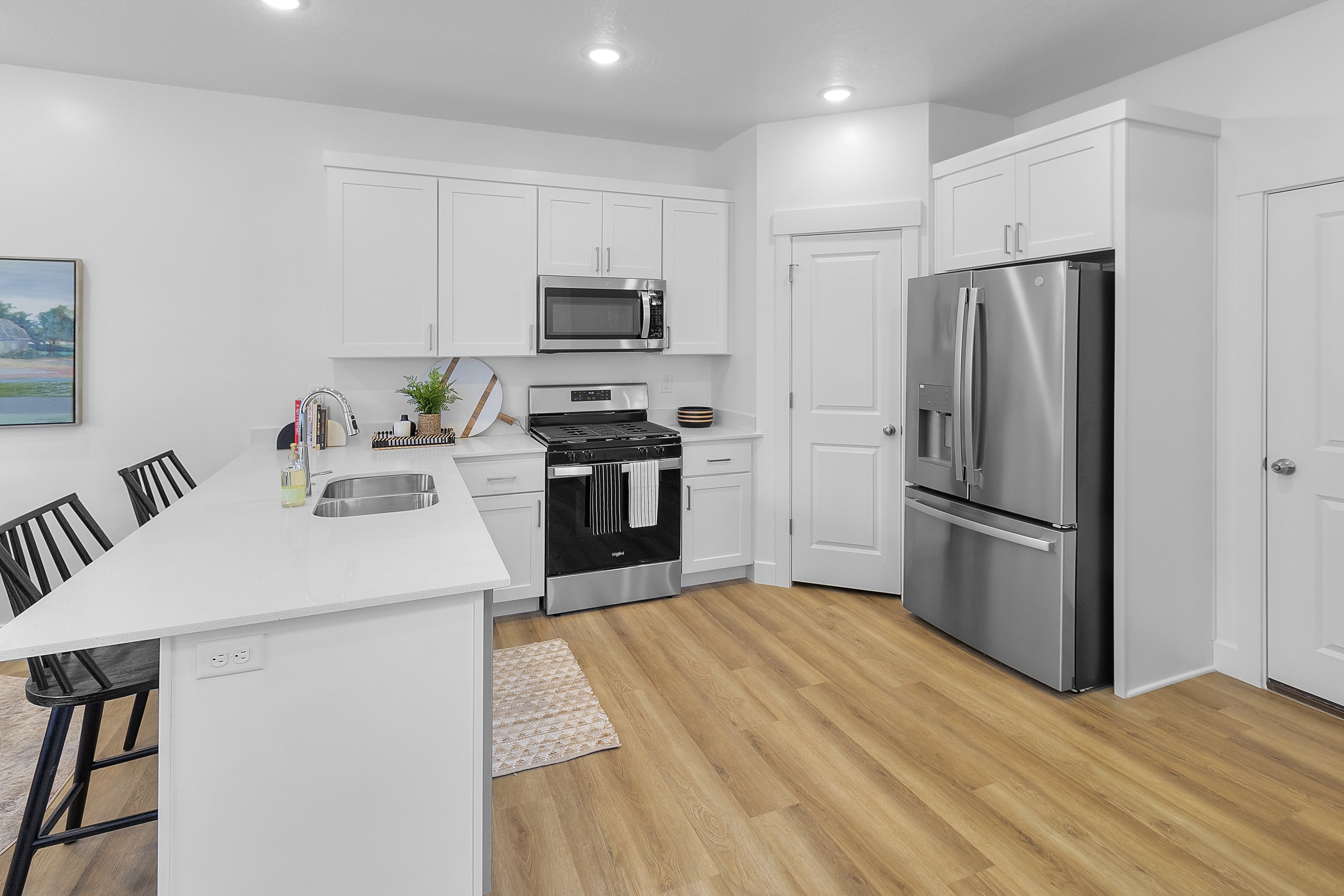 Kitchen featuring an island with an undermount sink, white cabinetry, stainless steel appliances, and wood-finish flooring