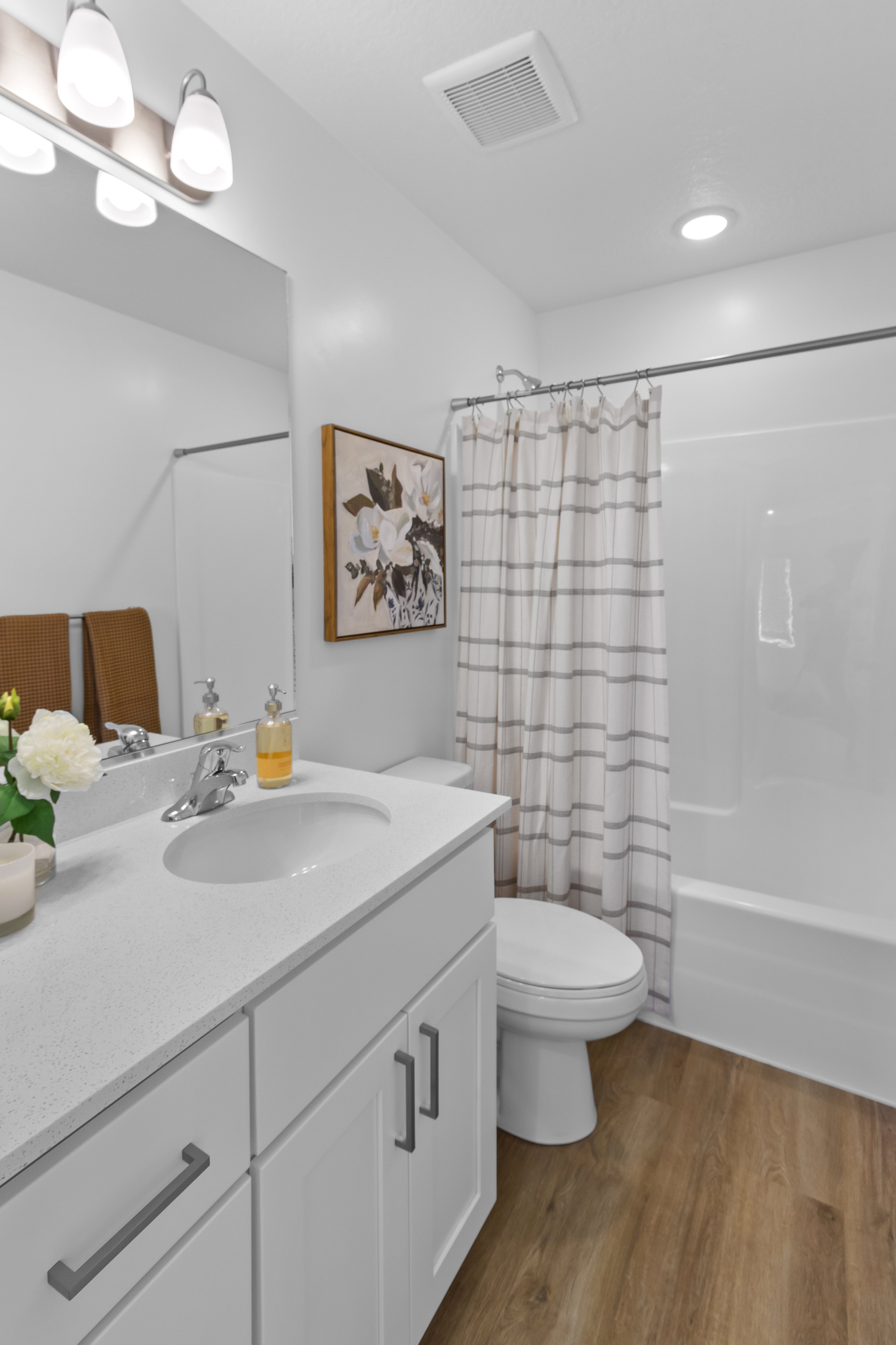 Contemporary bathroom featuring a white vanity with an integrated sink, a matching white countertop, and wood-finish flooring