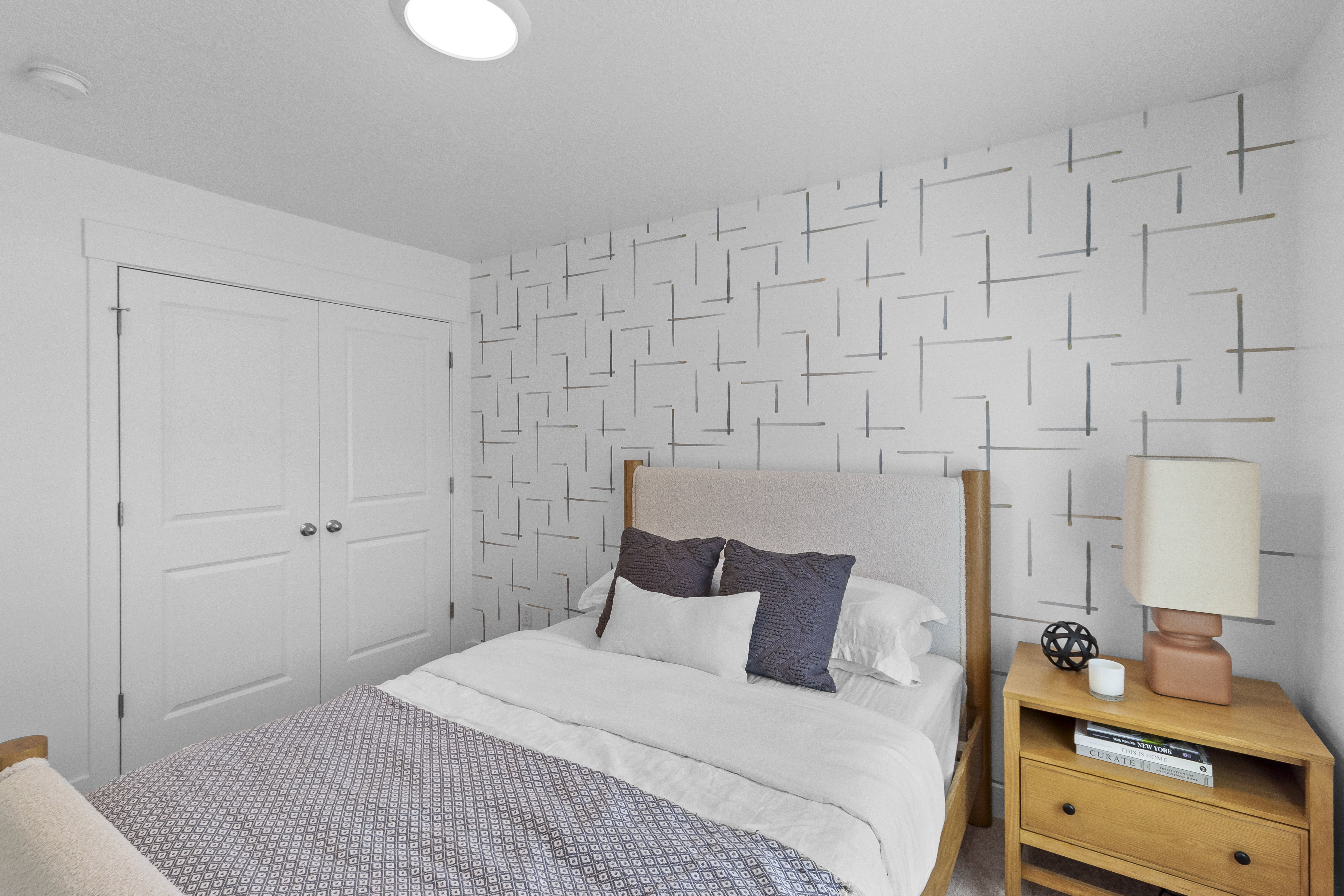 Bright bedroom featuring a patterned accent wall, recessed ceiling light, and a two-panel bifold closet door