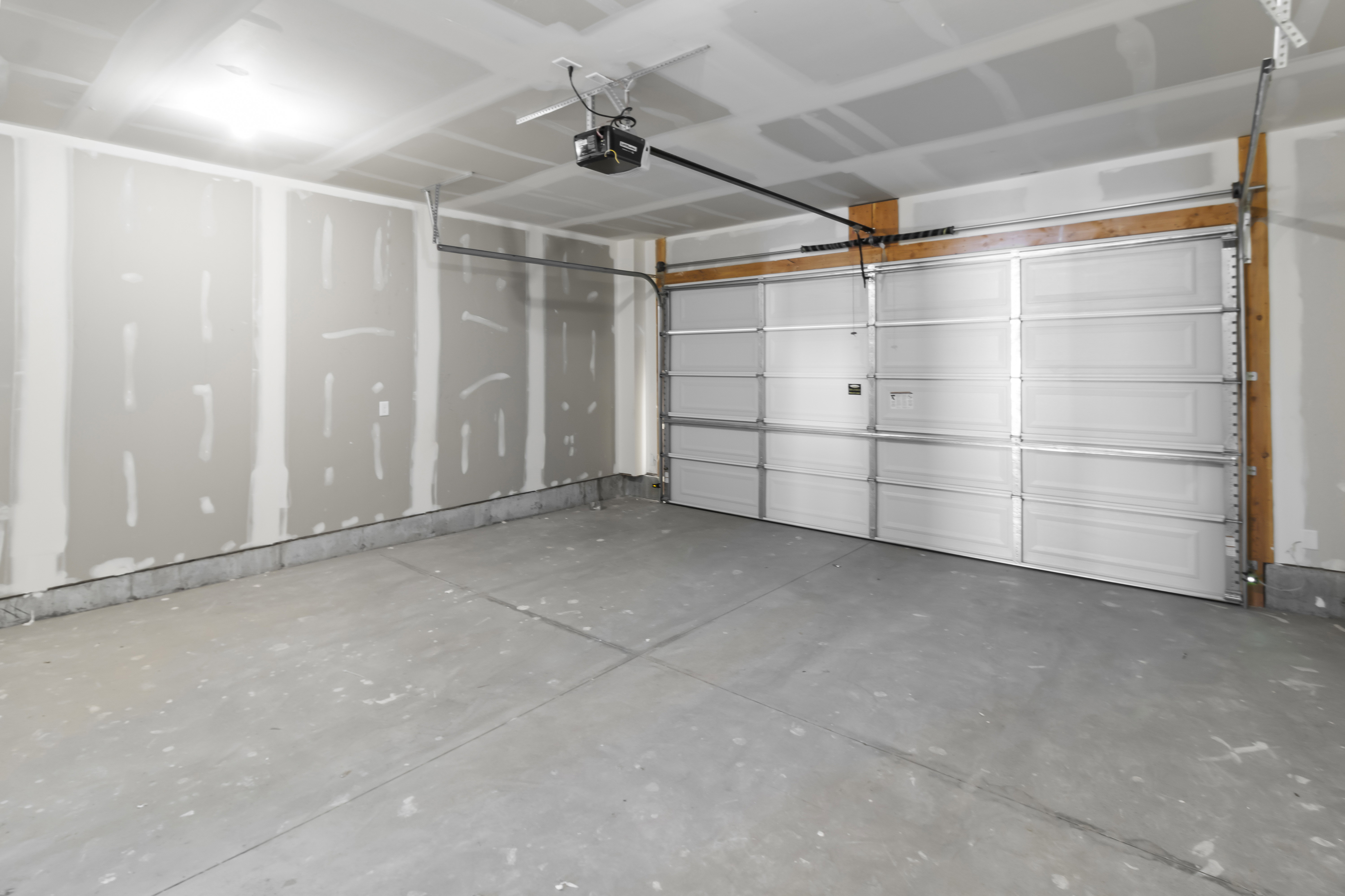 Spacious two-car garage featuring a sectional overhead door with an automatic opener, concrete flooring, and unfinished drywall walls ready for customization