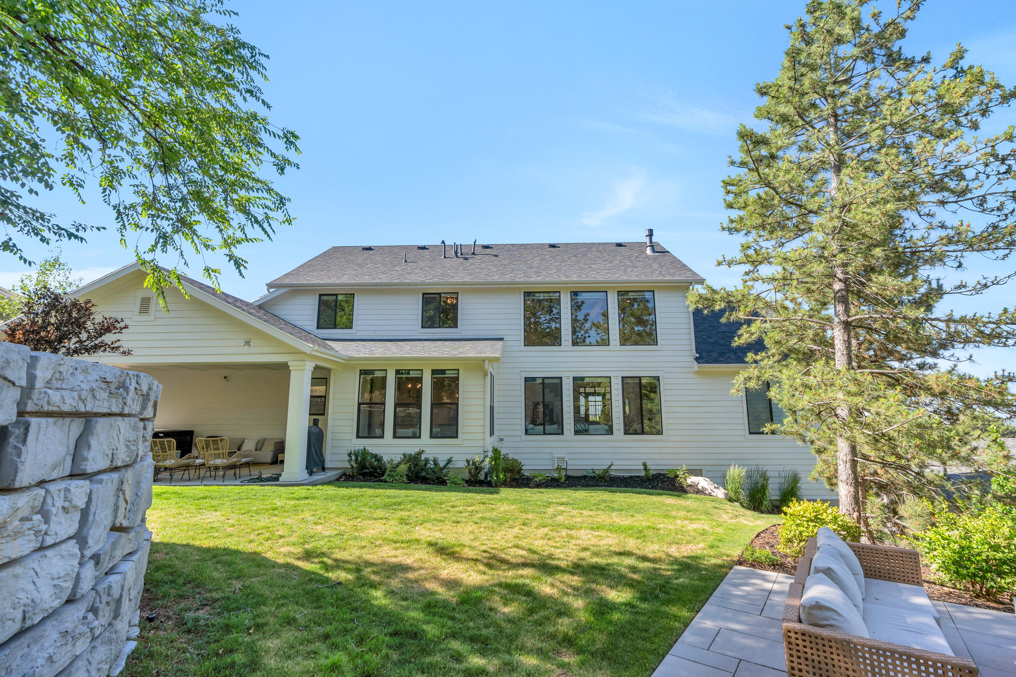 Expansive rear facade featuring a covered patio, multiple large windows, and a manicured lawn