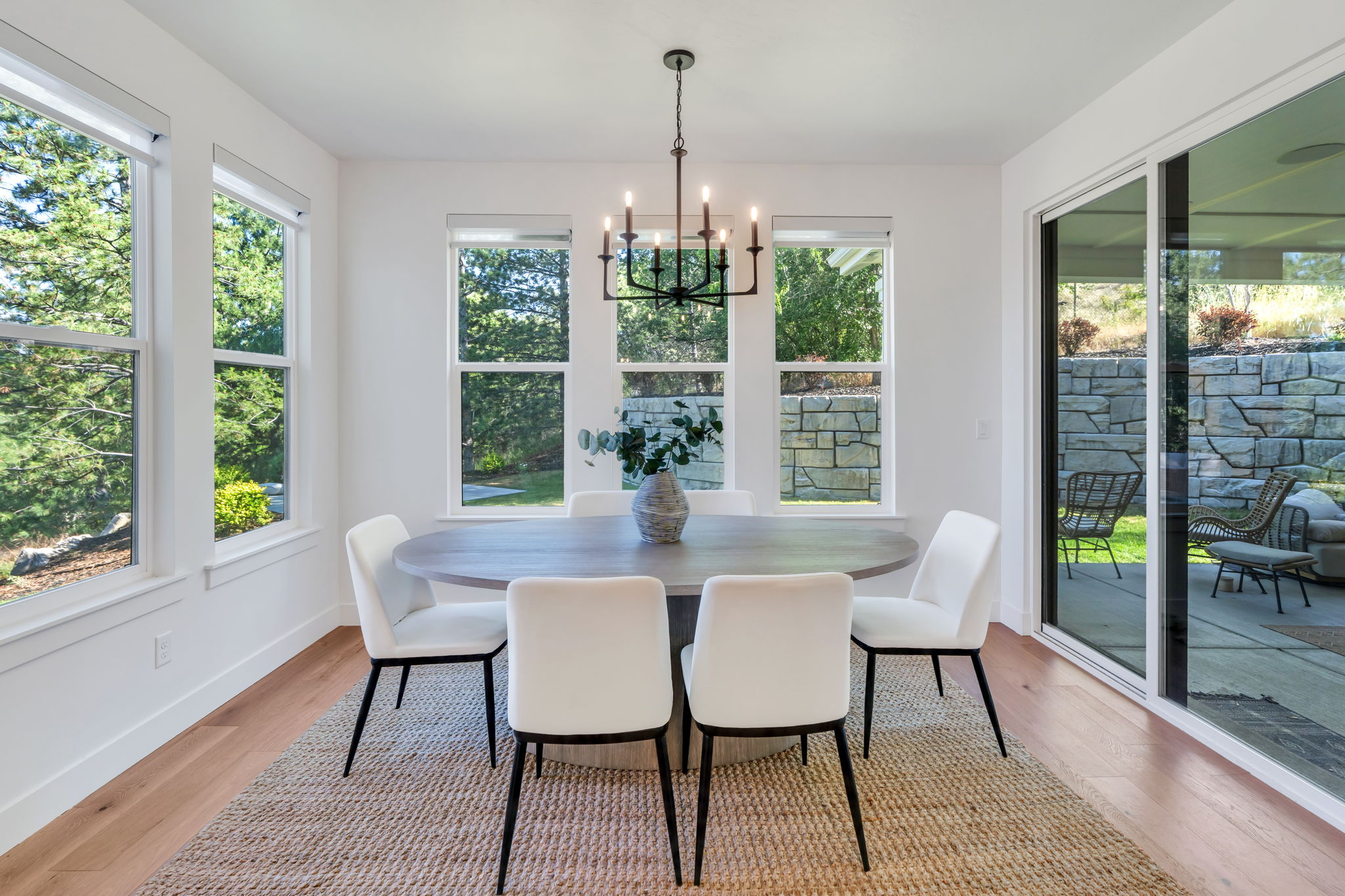 Bright dining area featuring hardwood-finish flooring, multiple windows, a sliding glass door, and a black wrought-iron chandelier