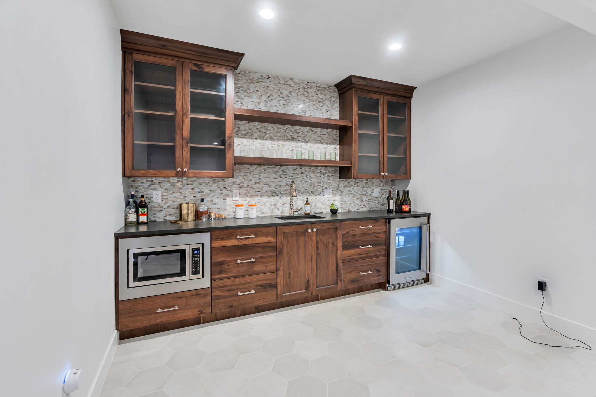 Built-in beverage station featuring custom wood cabinetry, dark countertops, a mosaic tile backsplash, recessed lighting, and hexagon tile flooring
