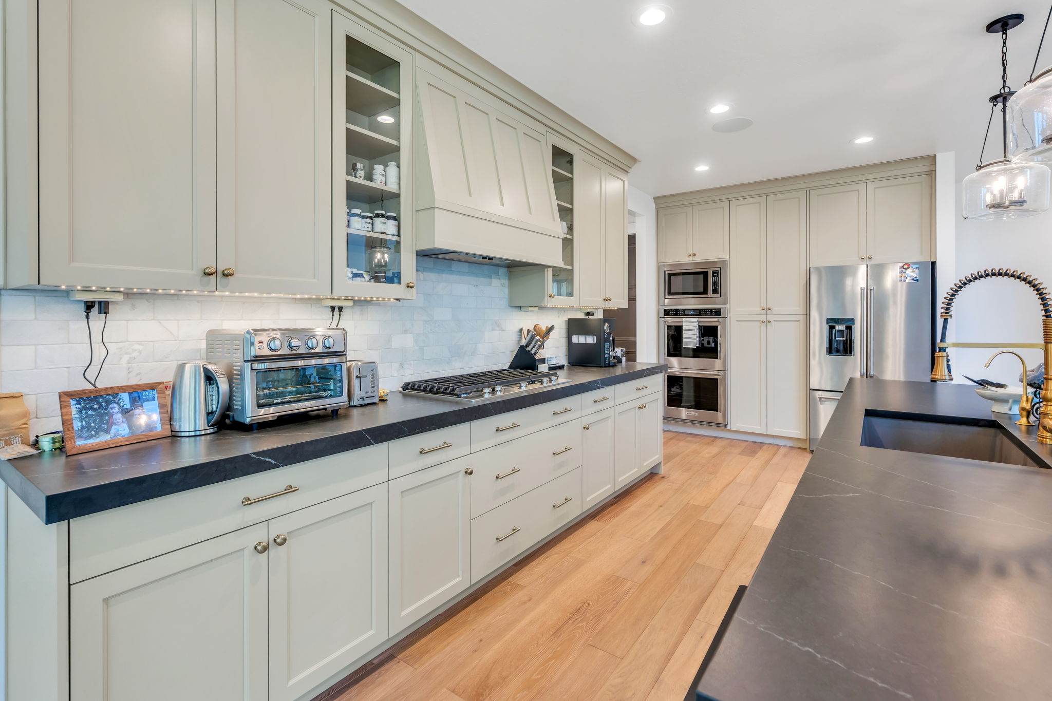 Light-toned cabinetry, dark countertops, a gas range, a large stainless steel refrigerator, and wood-finish flooring define this kitchen