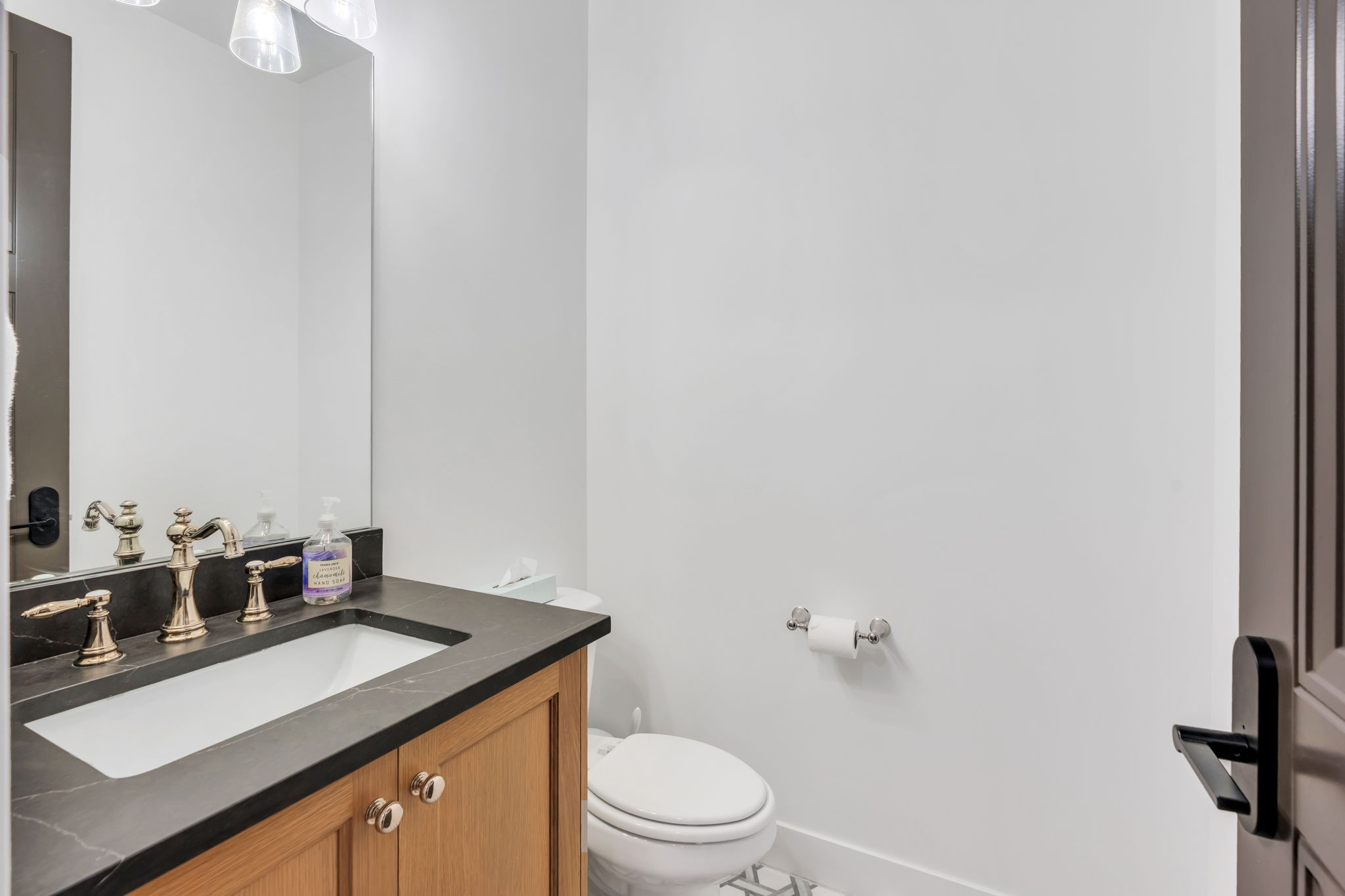 Bathroom featuring a wood-finish vanity with a dark stone countertop, an undermount sink, and a three-piece brass faucet