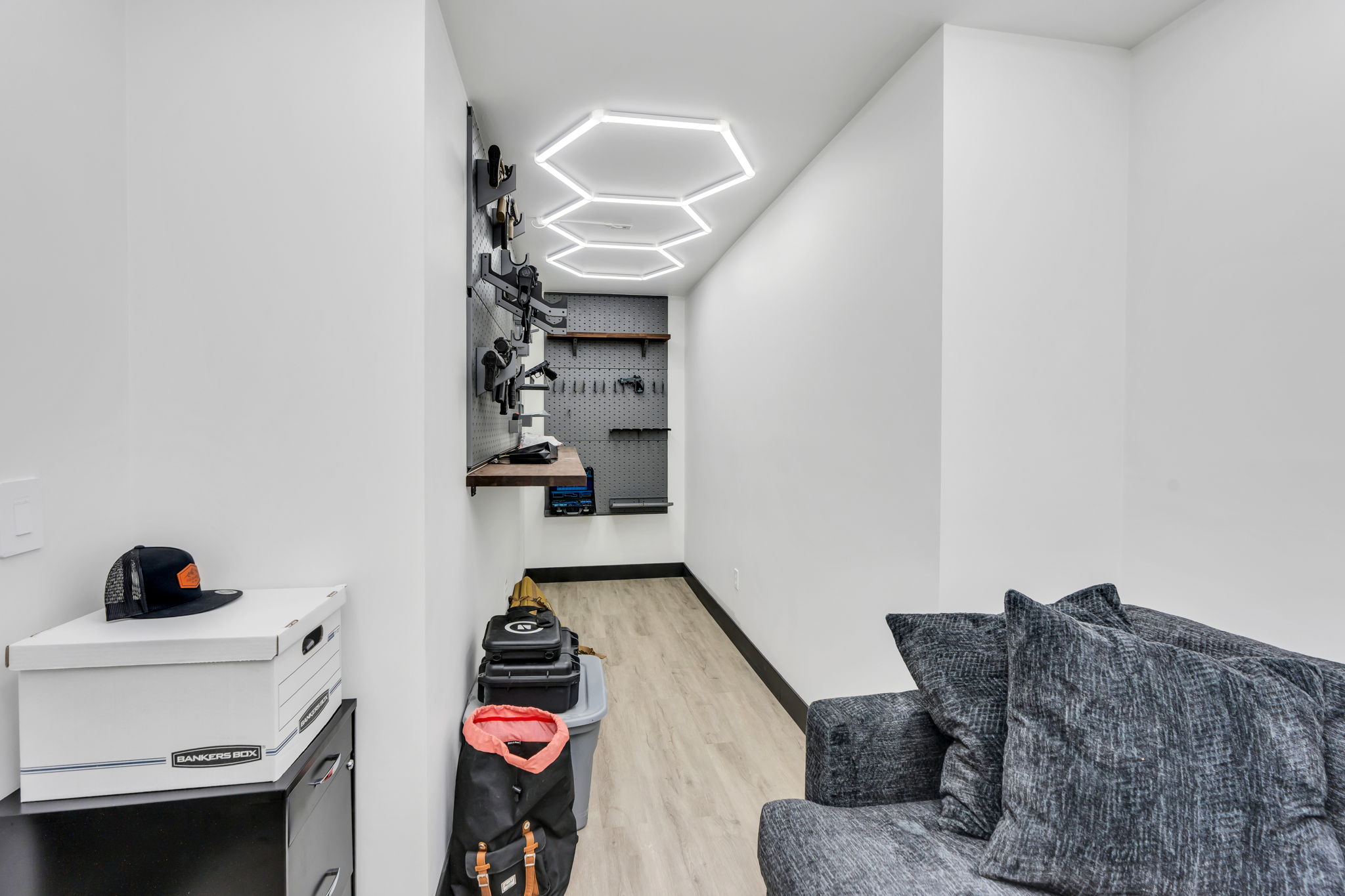 Specialized room featuring hexagonal ceiling lighting, engineered wood-finish flooring, and a comprehensive wall-mounted storage system with pegboard backing