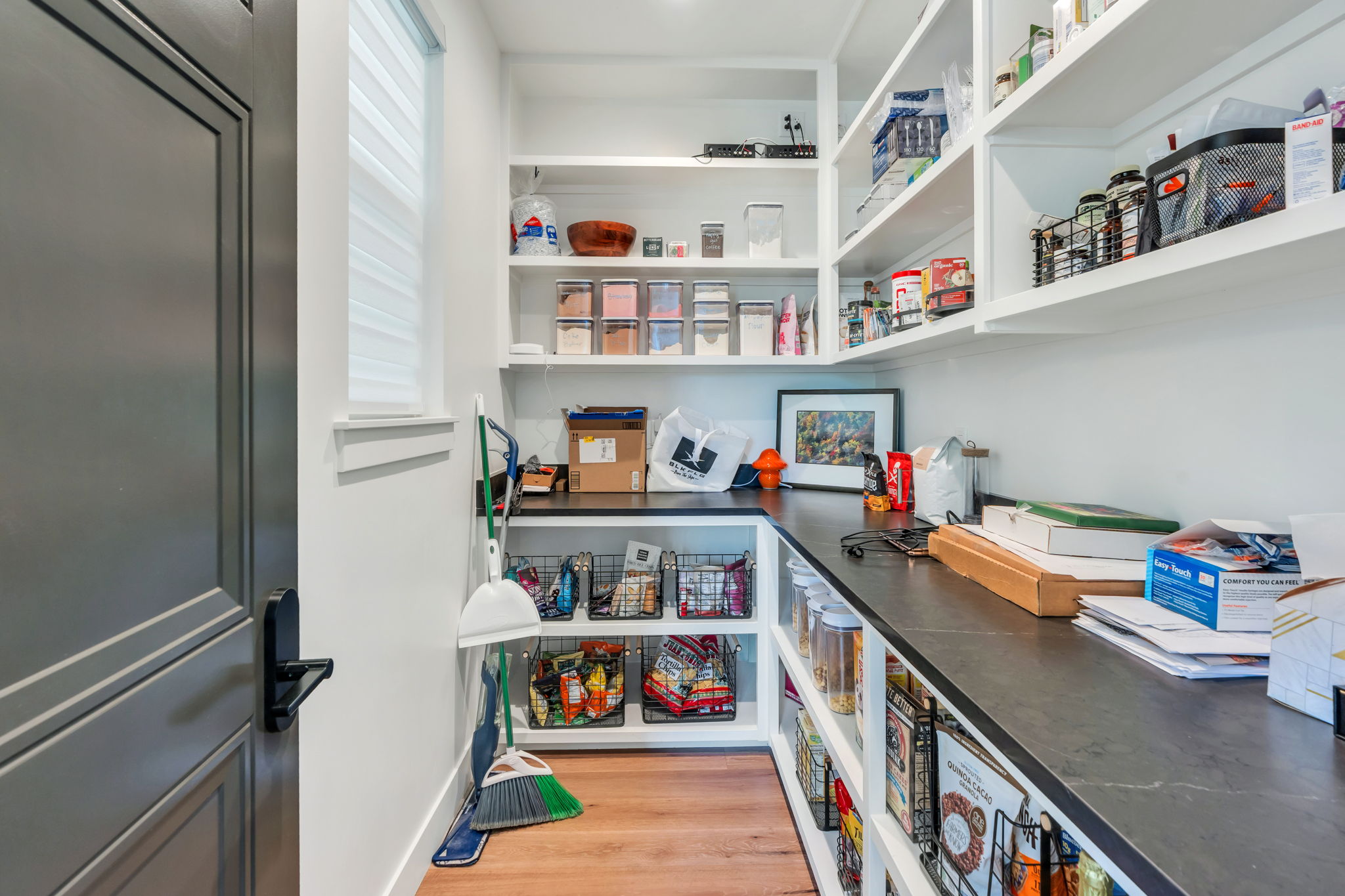 Well-appointed pantry featuring extensive built-in shelving, dark countertops, and wood-finish flooring