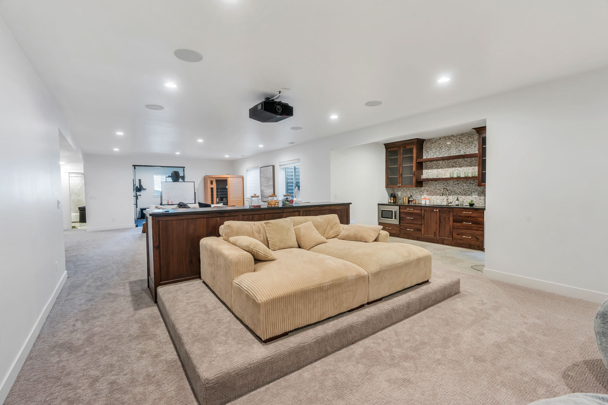 Carpeted entertainment area featuring a raised platform, built-in media projector, recessed ceiling lighting, and integrated ceiling speakers