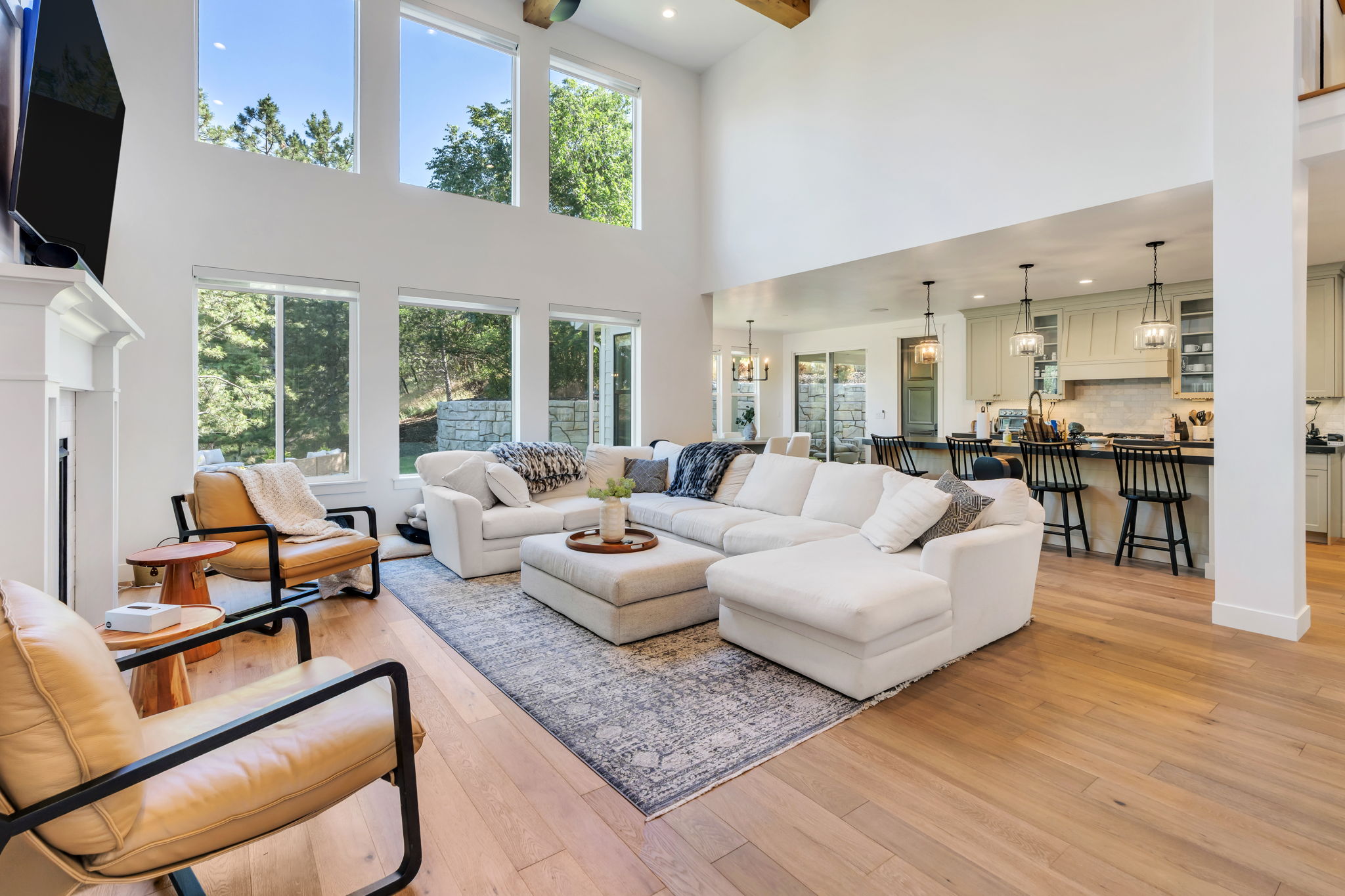 Soaring ceilings define this spacious living area, featuring abundant natural light from multiple large windows and a white-painted fireplace mantel