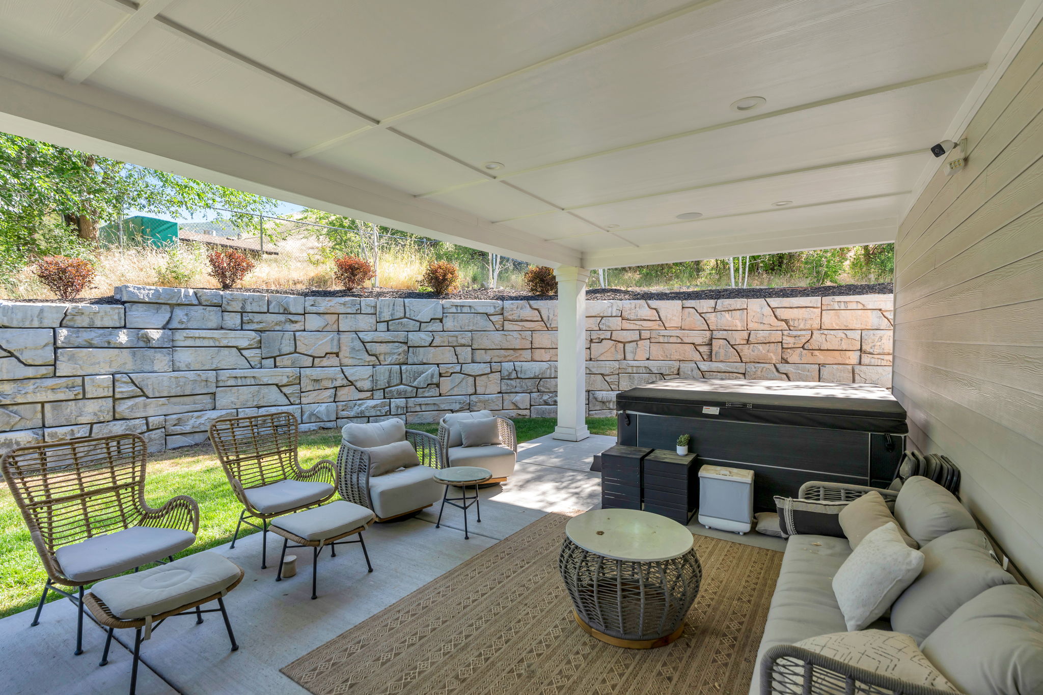 Covered patio with recessed lighting, stone retaining wall, and integrated hot tub