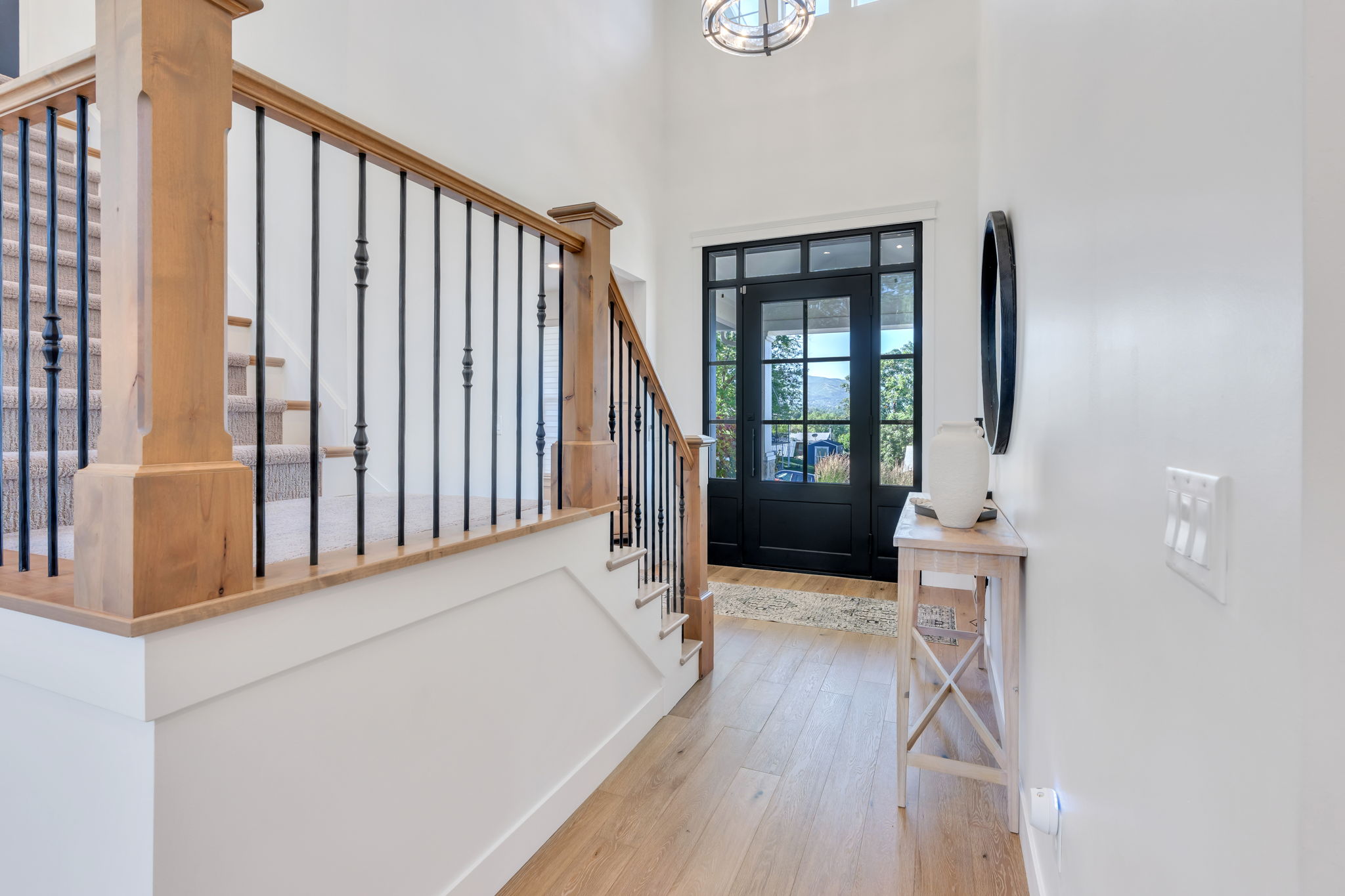 Entryway featuring a black-framed glass panel door, wood-finish flooring, and a grand staircase with wood newel posts and black iron balusters
