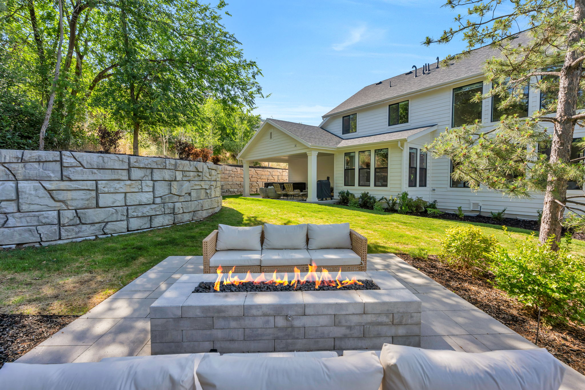 Expansive outdoor living area featuring a built-in fire pit, stone paver patio, and a retaining wall