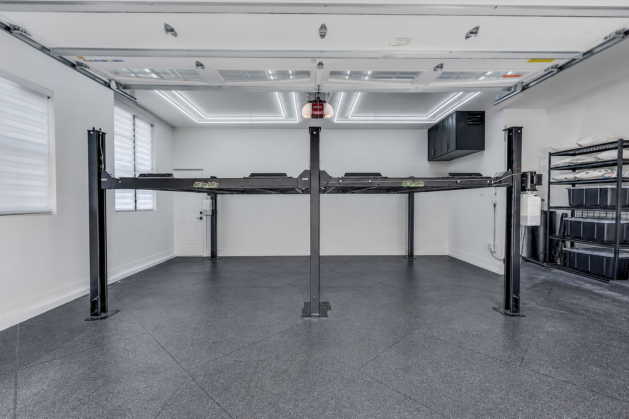 Garage space featuring a four-post vehicle lift, durable tile flooring, and integrated ceiling lighting