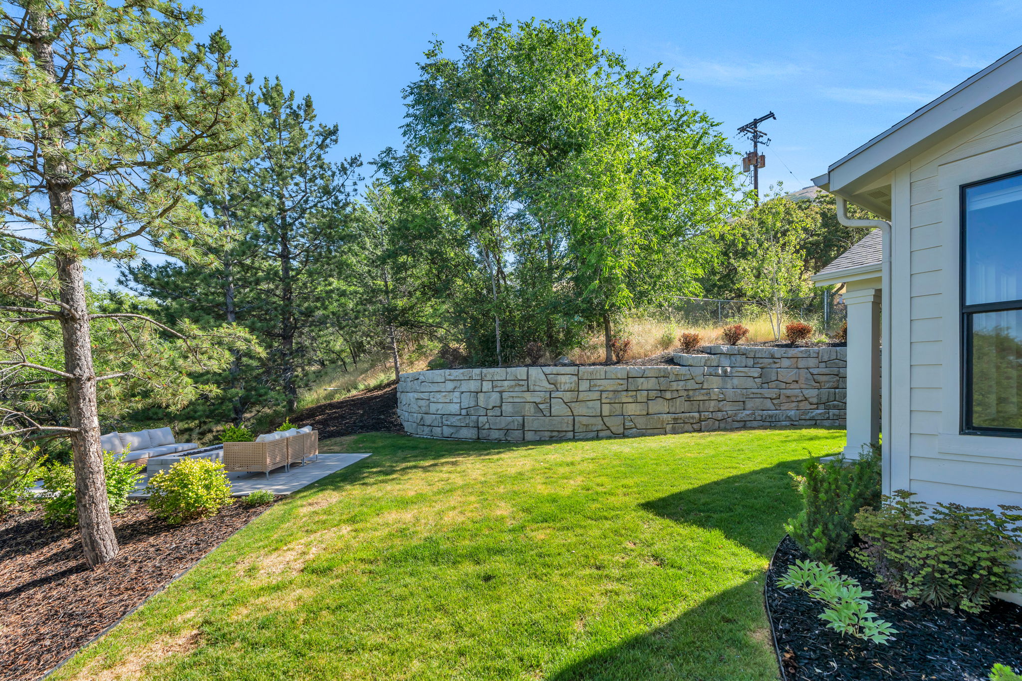 Expansive lawn with a stone retaining wall, mature trees, and a paved patio area