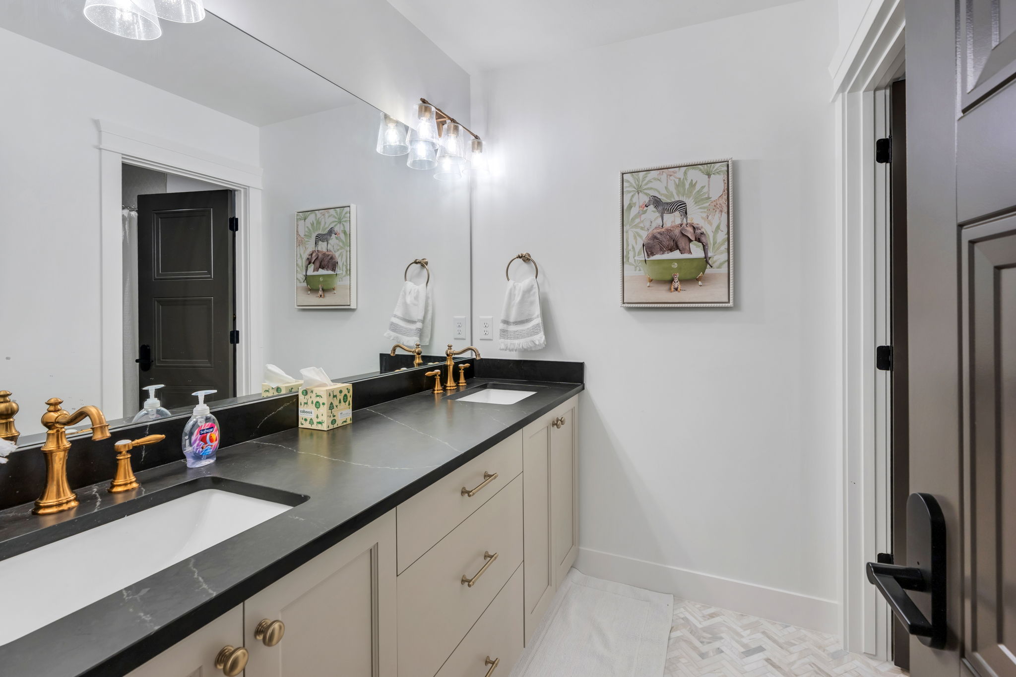 Bathroom featuring a dual vanity with undermount sinks, dark countertops, brass-finish fixtures, and herringbone tile flooring
