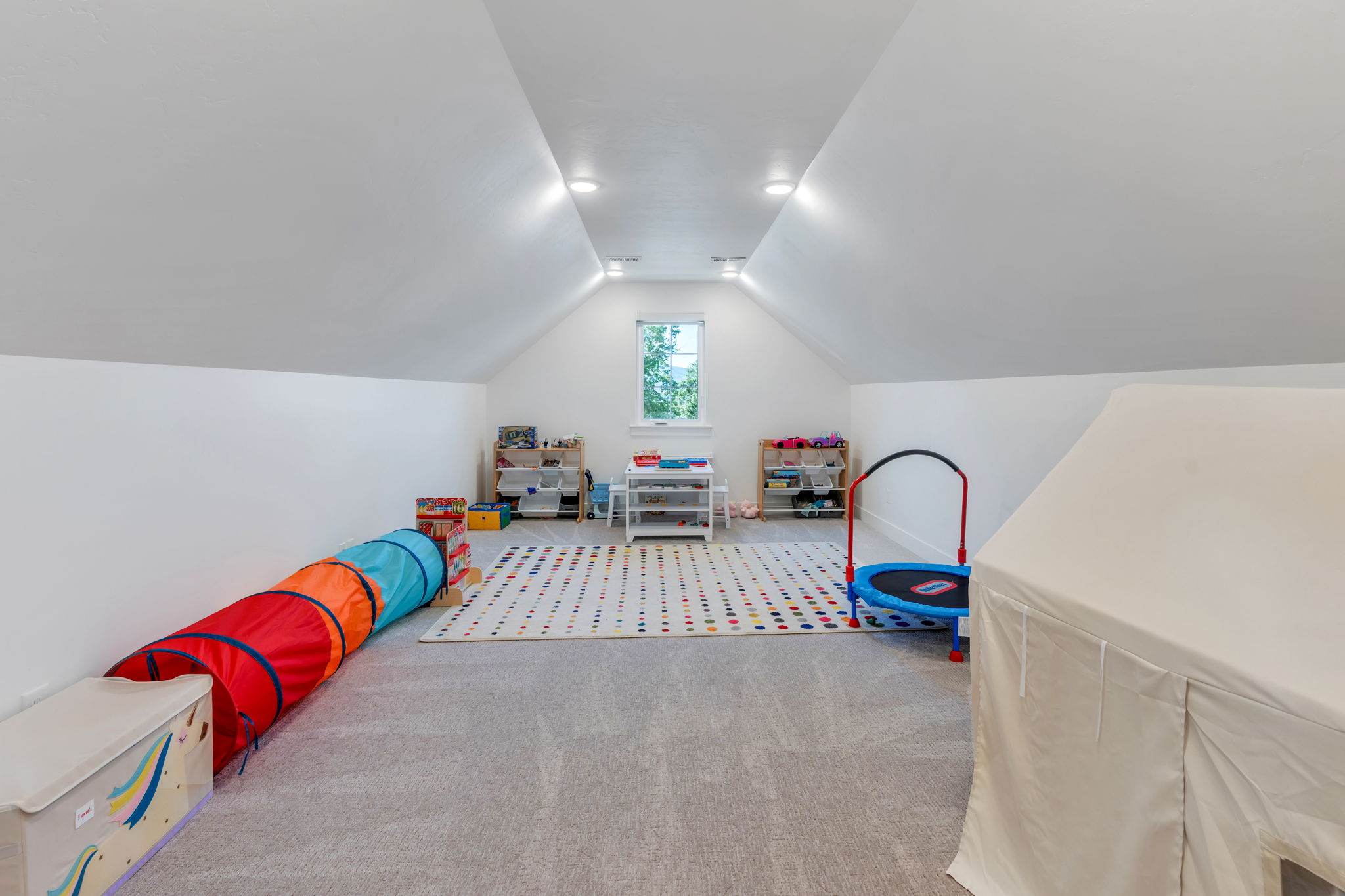 Bright attic space featuring sloped ceilings, recessed lighting, and a window for natural illumination