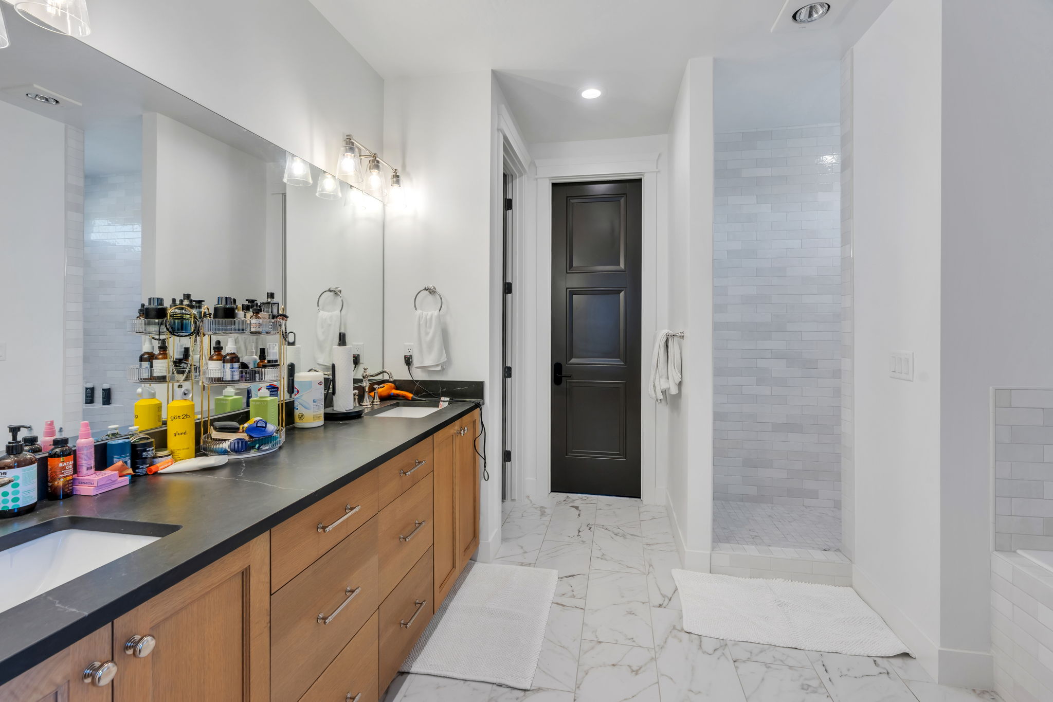 Spacious bathroom featuring a dual vanity with a dark countertop and wood-finish cabinetry