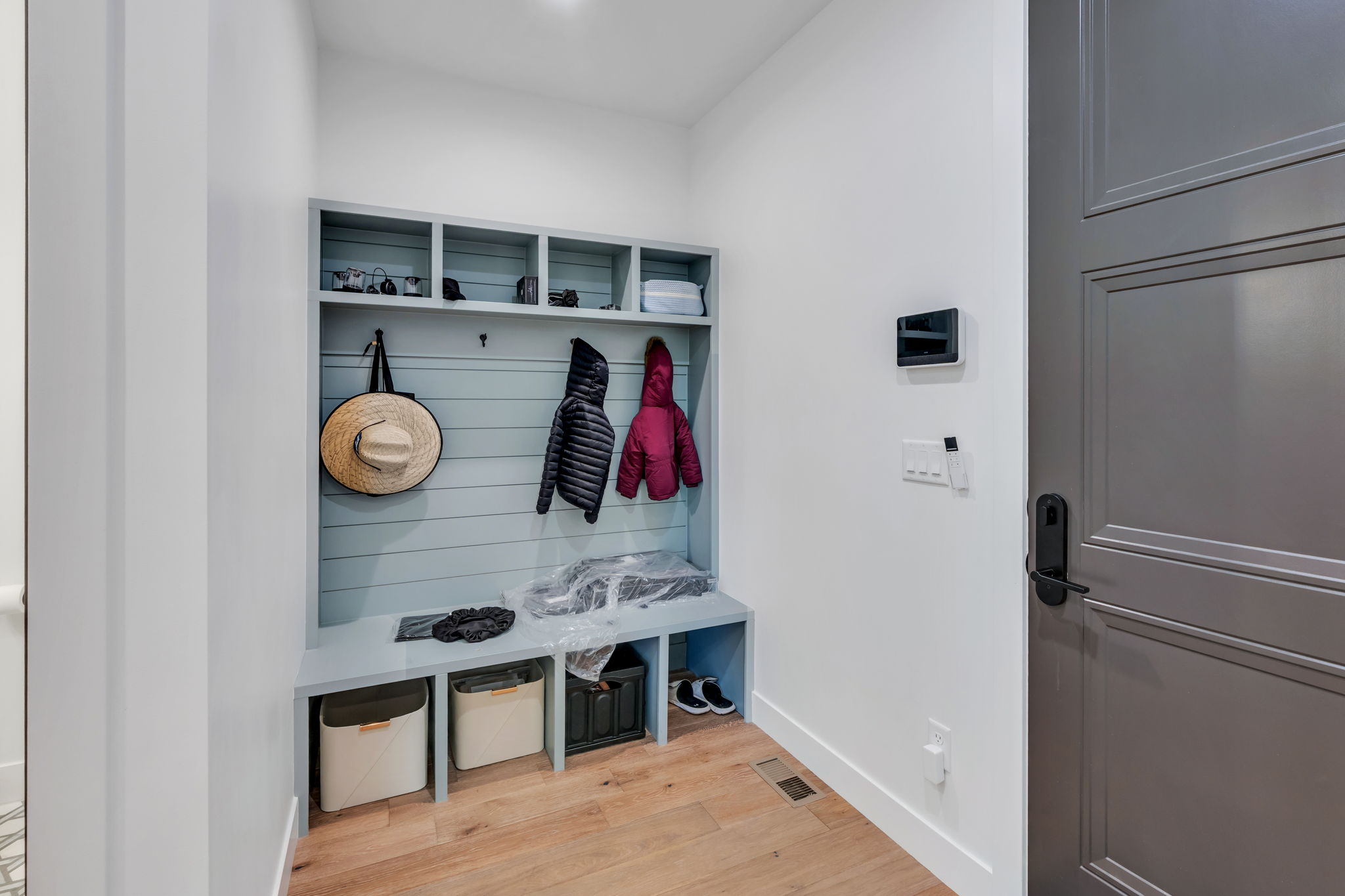 Built-in mudroom bench with cubbies and coat hooks, wood-finish flooring, white walls, and a paneled door with matte black hardware