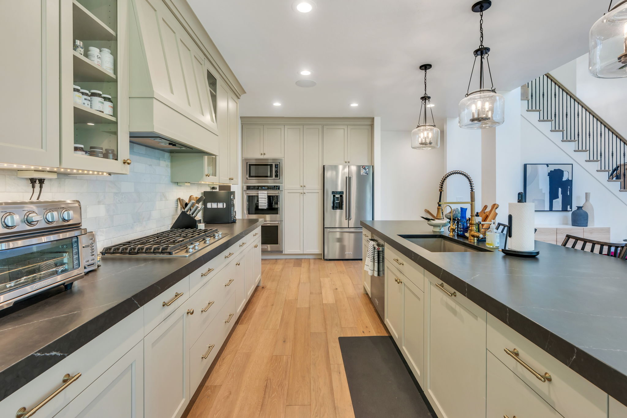 Contemporary kitchen featuring a large central island with an undermount sink, pendant lighting, light-toned cabinetry, dark countertops, and stainless steel appliances