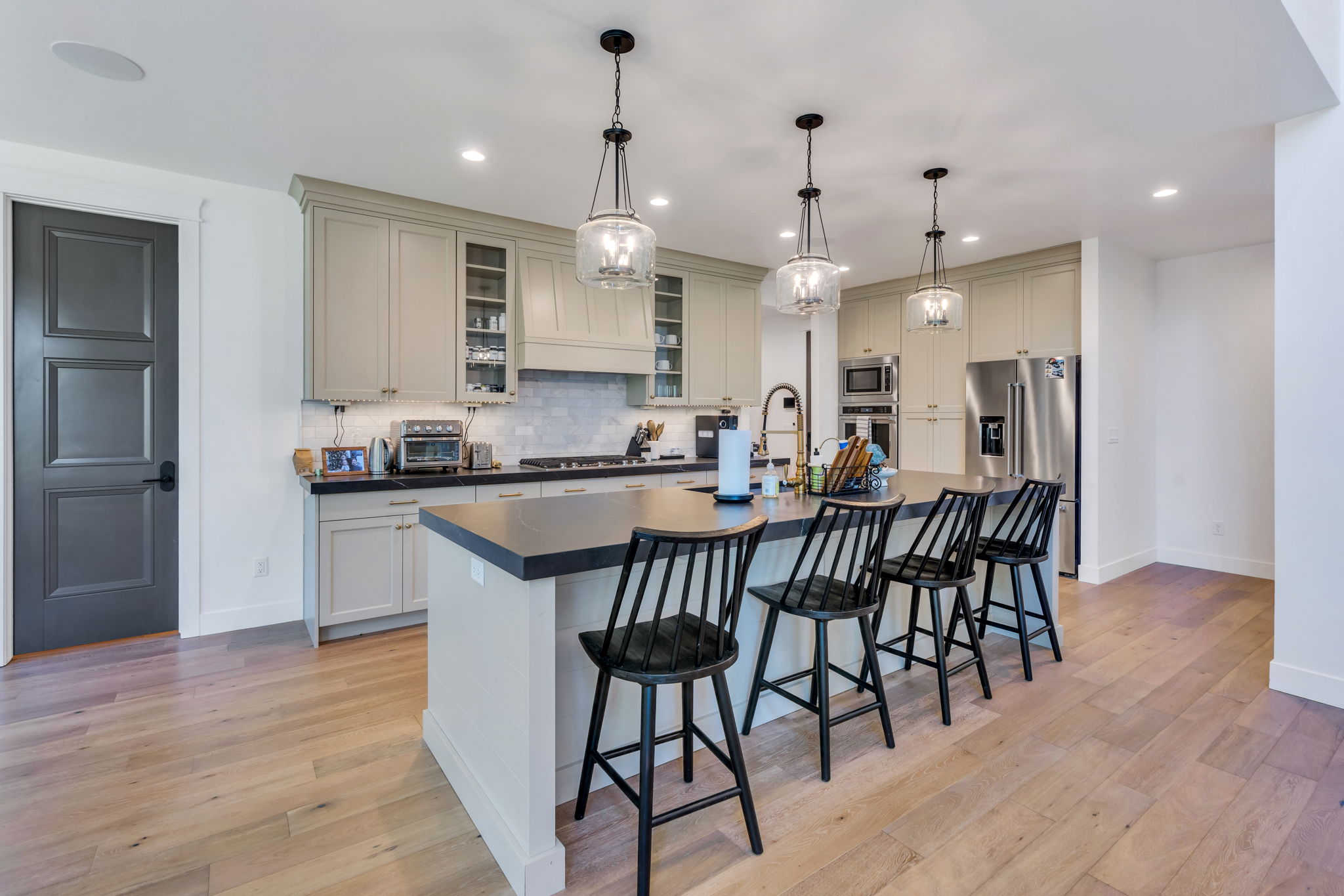 Gourmet kitchen featuring a large island with seating, stainless steel appliances, light-toned cabinetry, wood-finish flooring, and pendant lighting