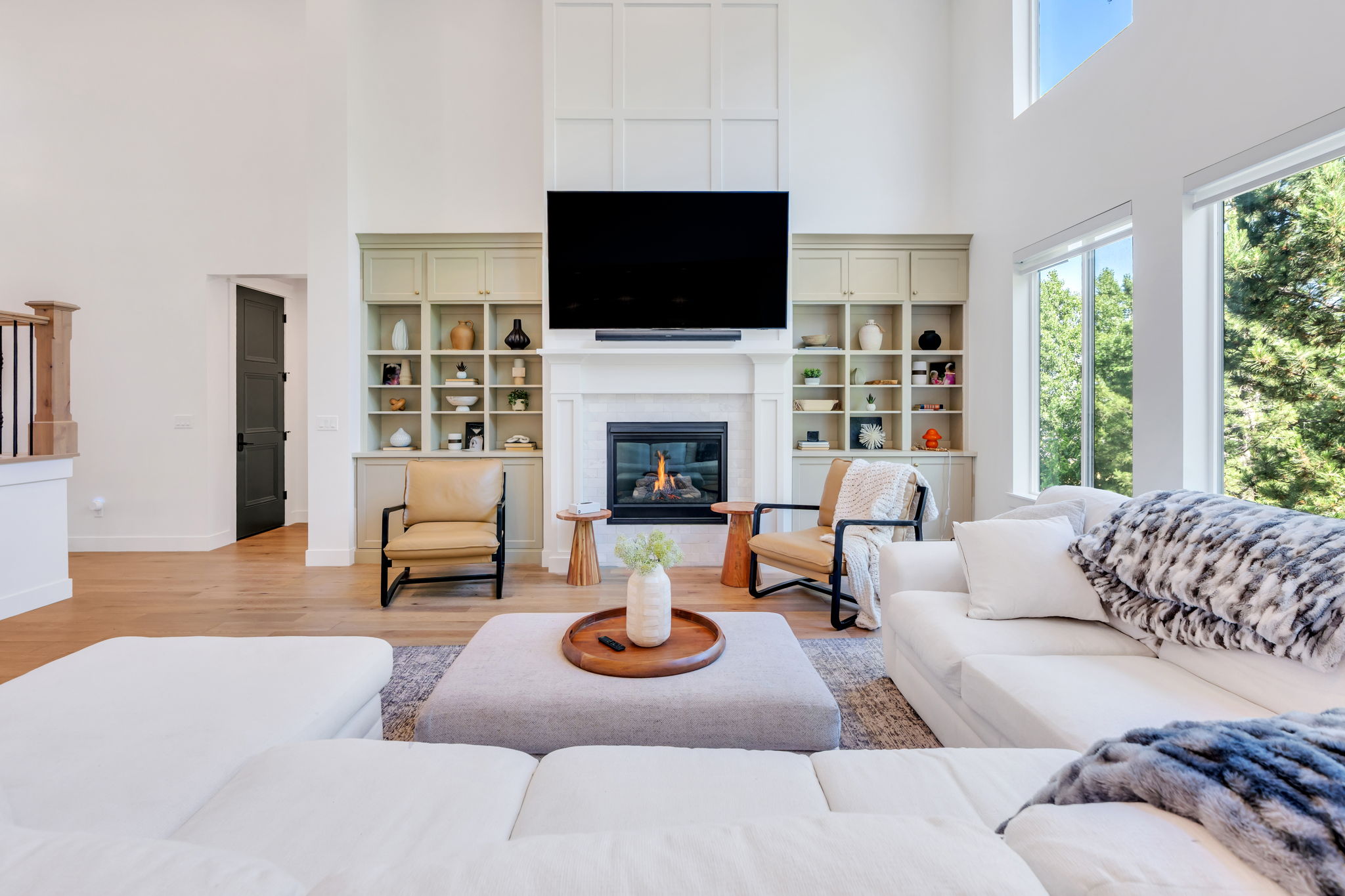 Spacious living area featuring a tall fireplace with a white mantel, built-in shelving, wood-finish flooring, and large windows
