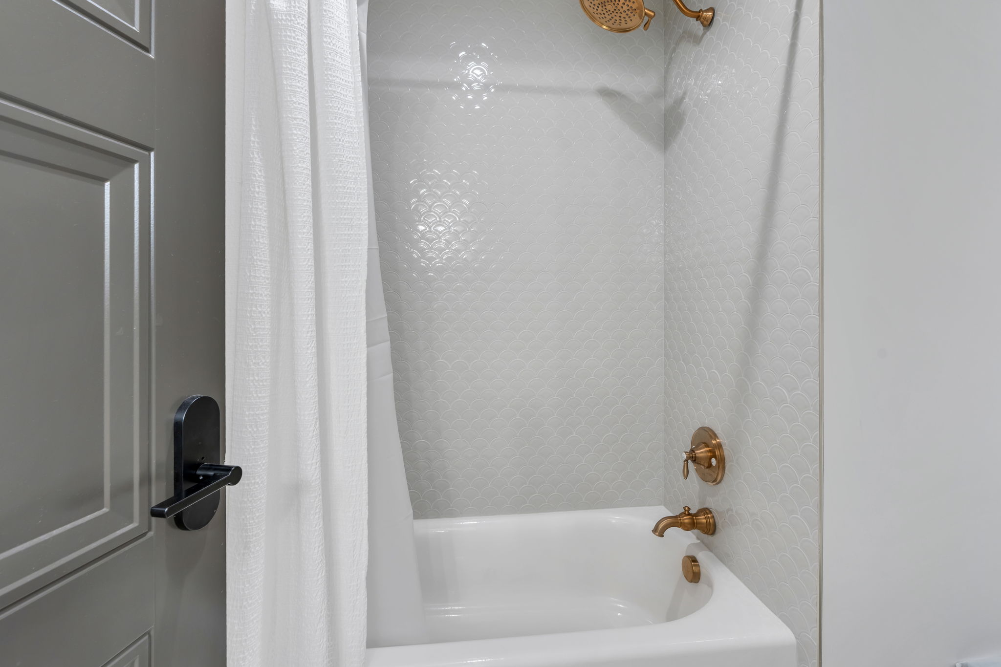 Bathtub with textured white wall tile and brass fixtures