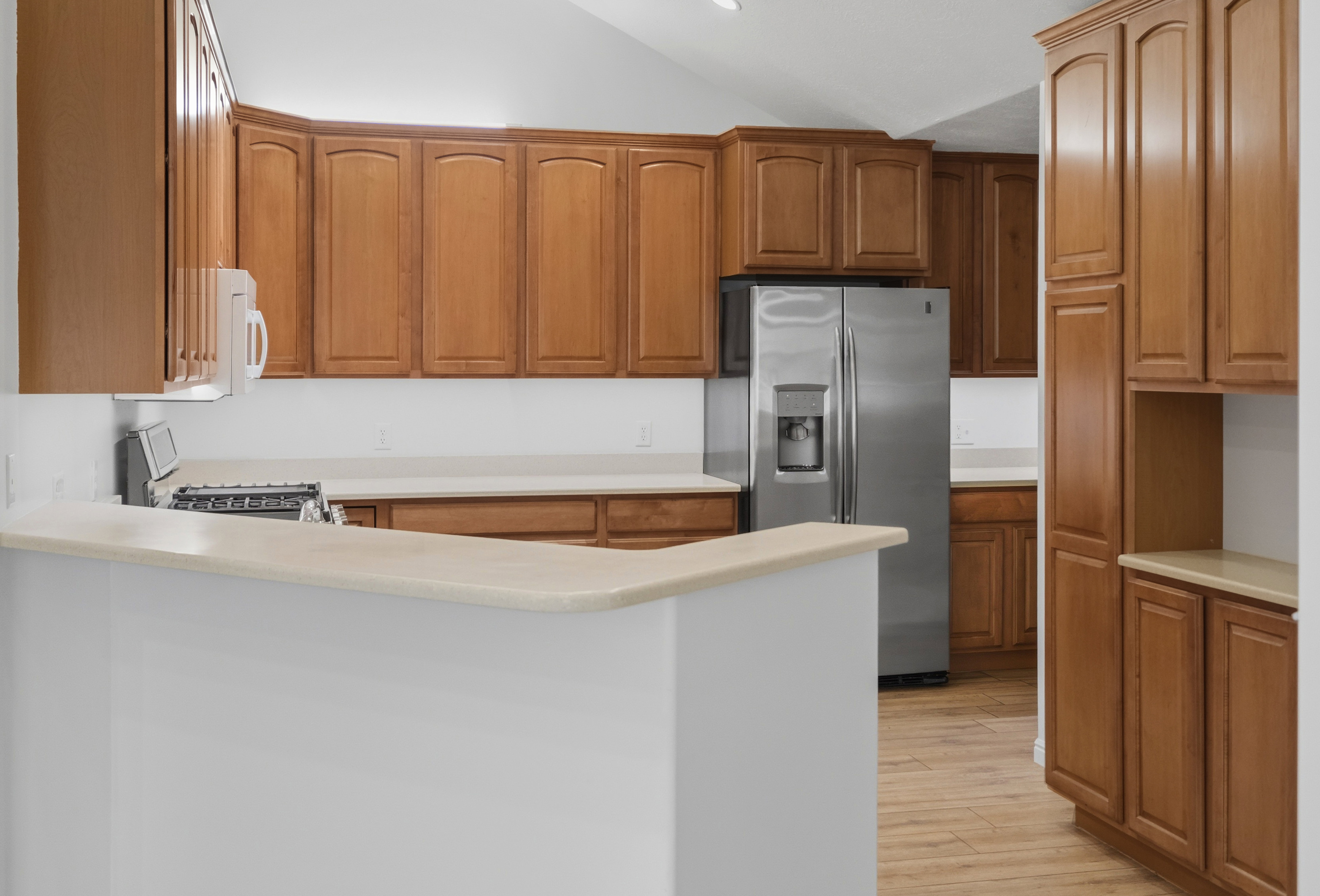 Kitchen featuring wood-finish cabinetry, stainless steel refrigerator, white countertops, built-in microwave, and wood-finish flooring