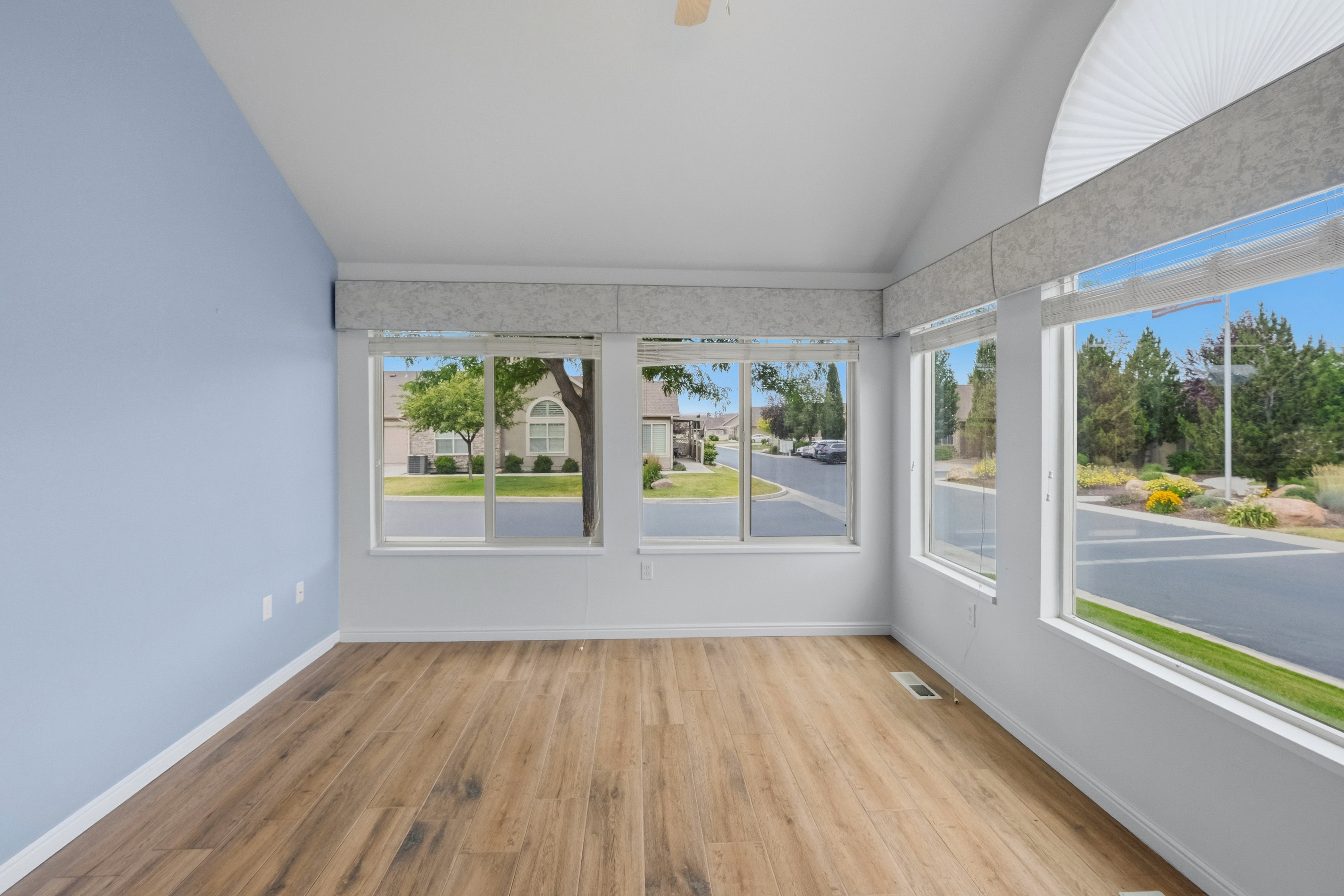 Vaulted ceiling with a ceiling fan, wood-finish flooring, and multiple windows