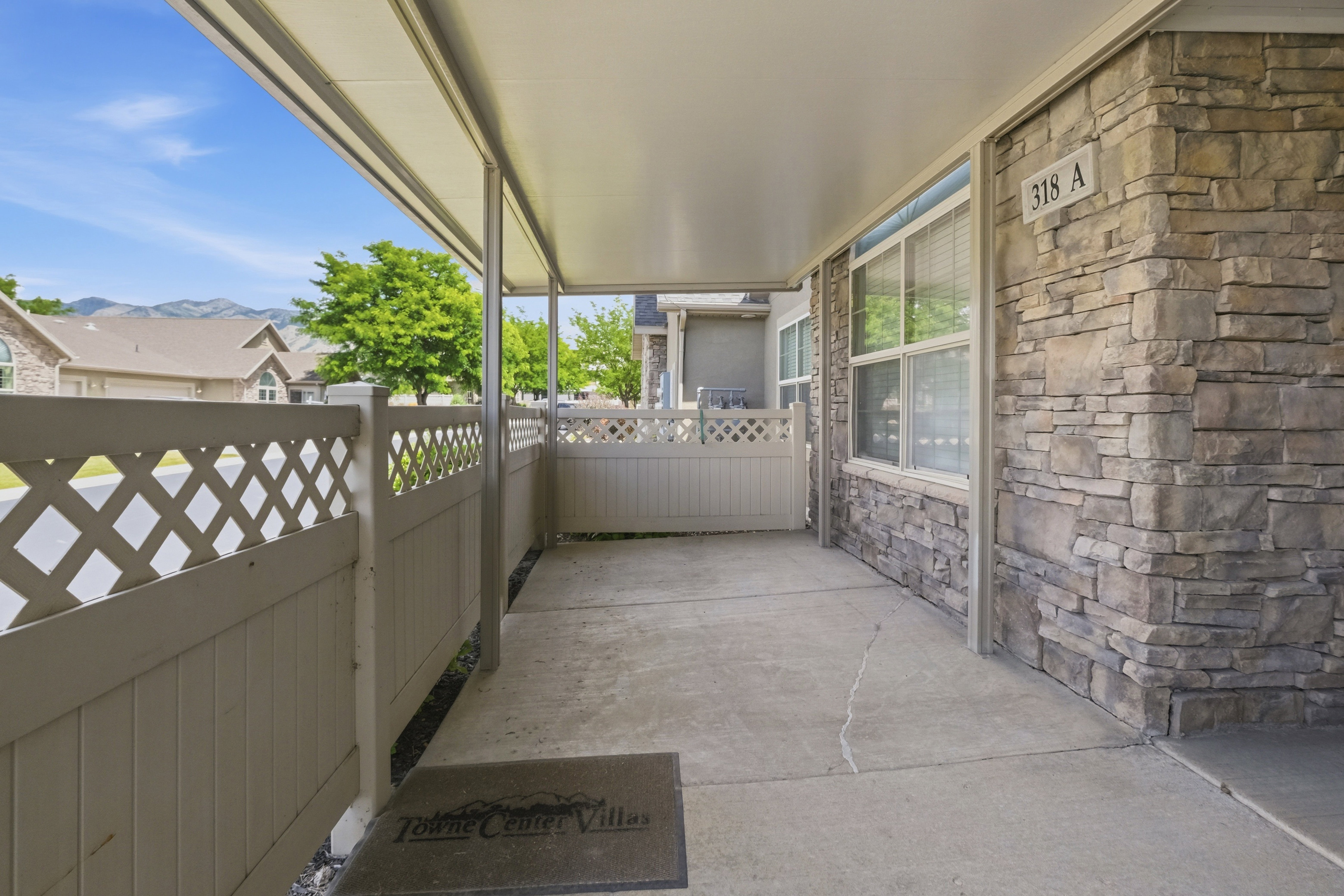 Covered concrete patio featuring a decorative lattice privacy fence and a stone facade exterior