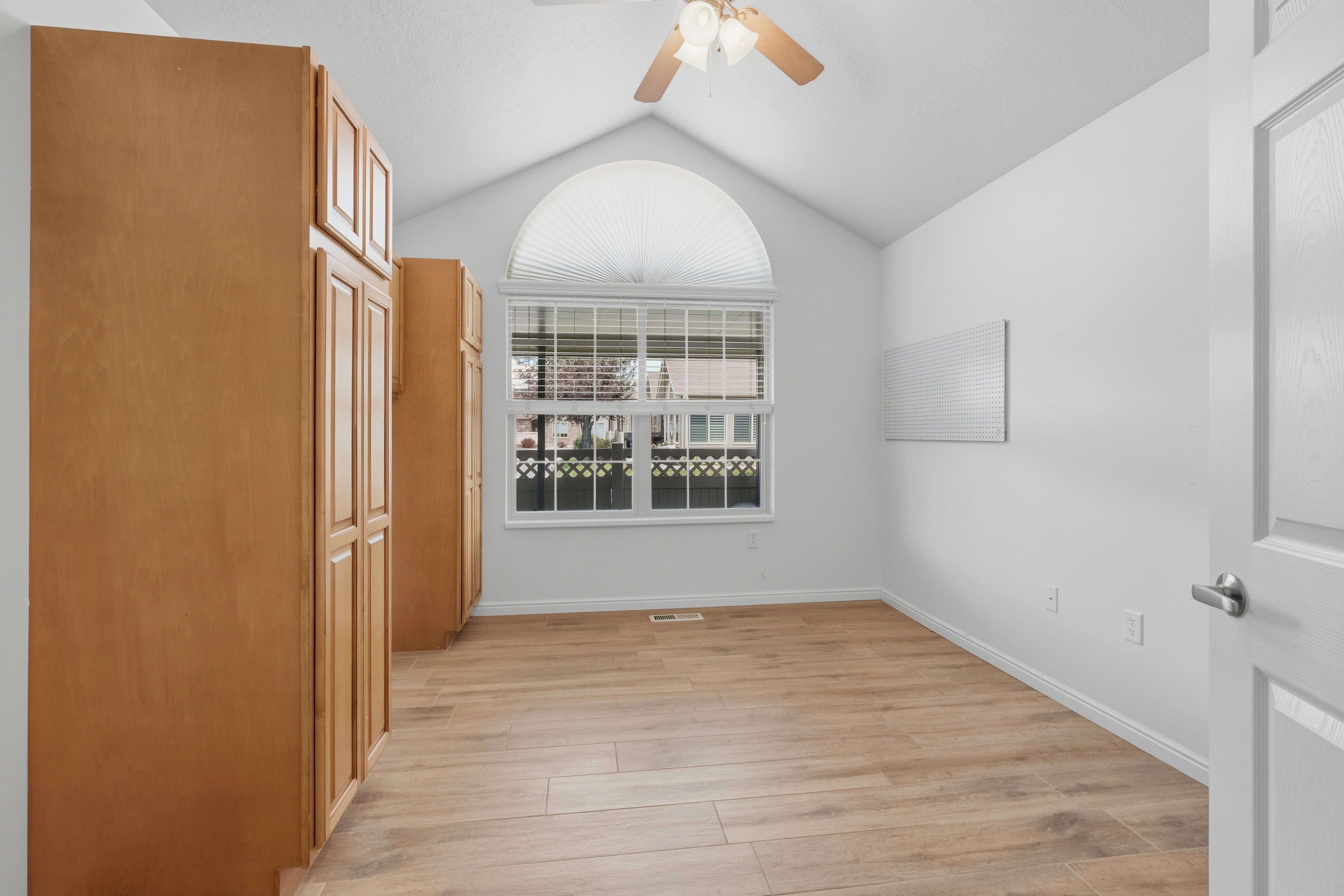Vaulted ceiling room featuring ample wood-finish cabinetry, a large window with an arched transom, and wood-look flooring
