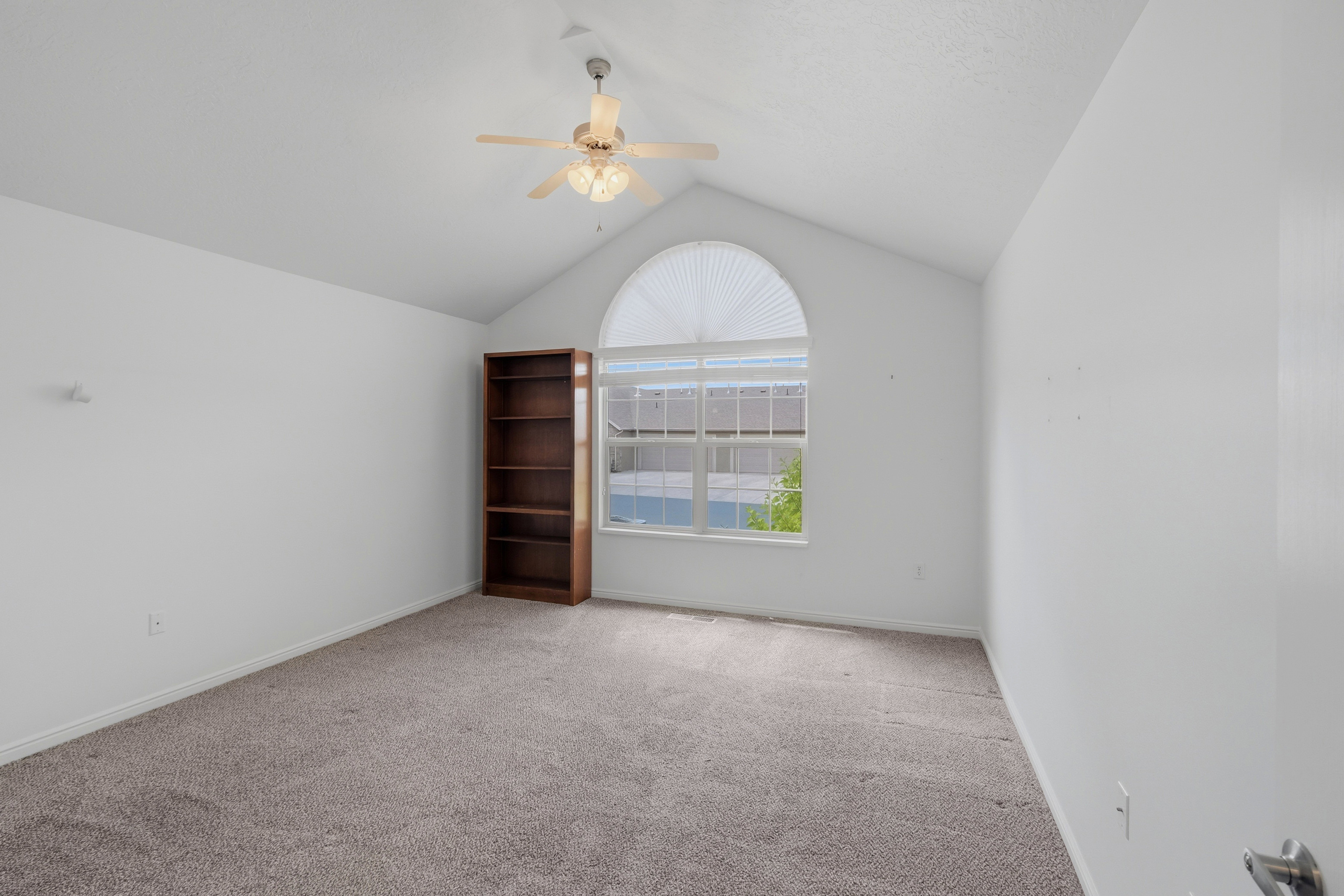 Room featuring a vaulted ceiling, an arched window with pleated blinds, and neutral carpeting