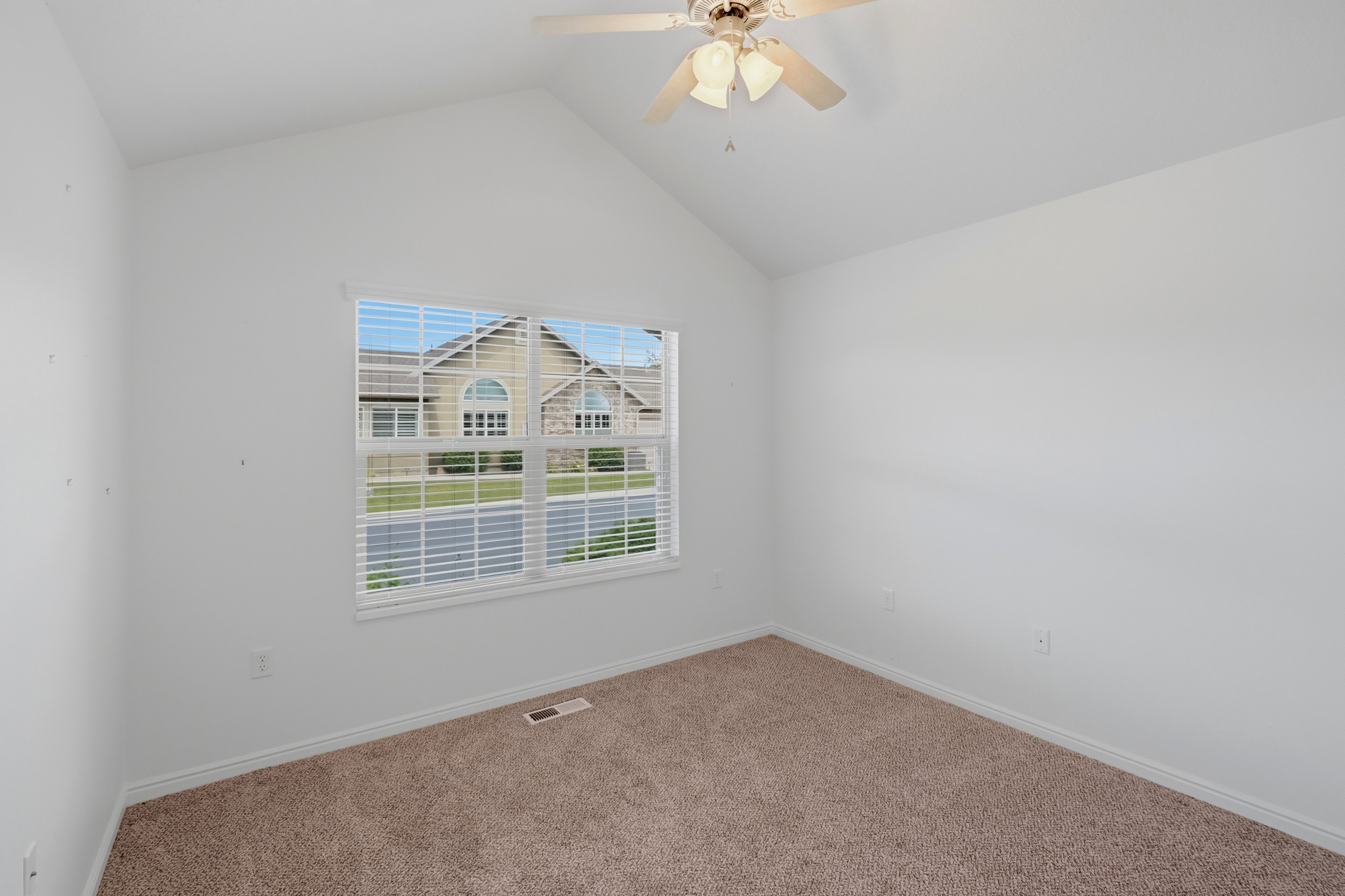 Vaulted ceiling room featuring a large window with blinds and carpeting