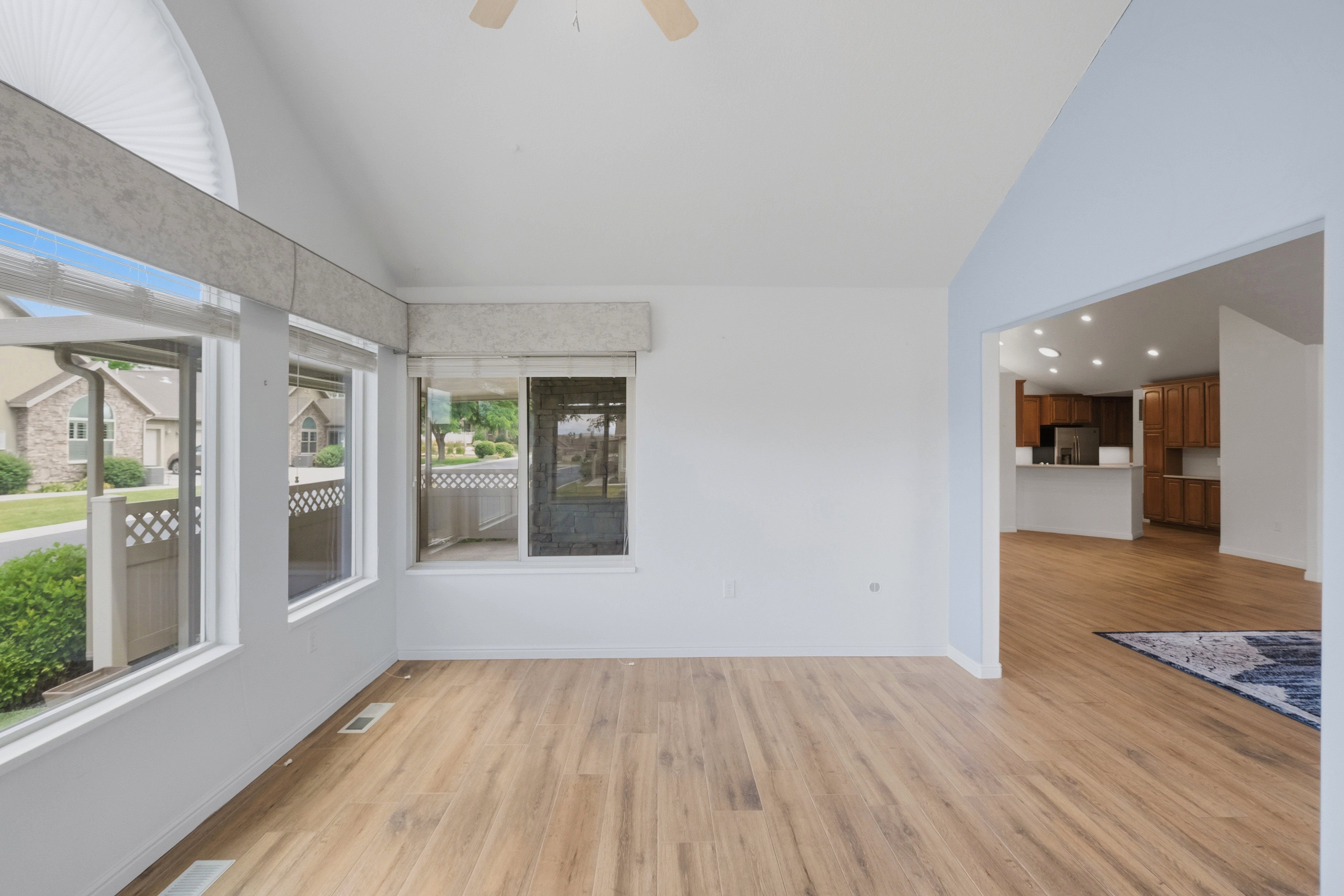 Vaulted ceiling space featuring wood-finish flooring, a ceiling fan, and multiple windows