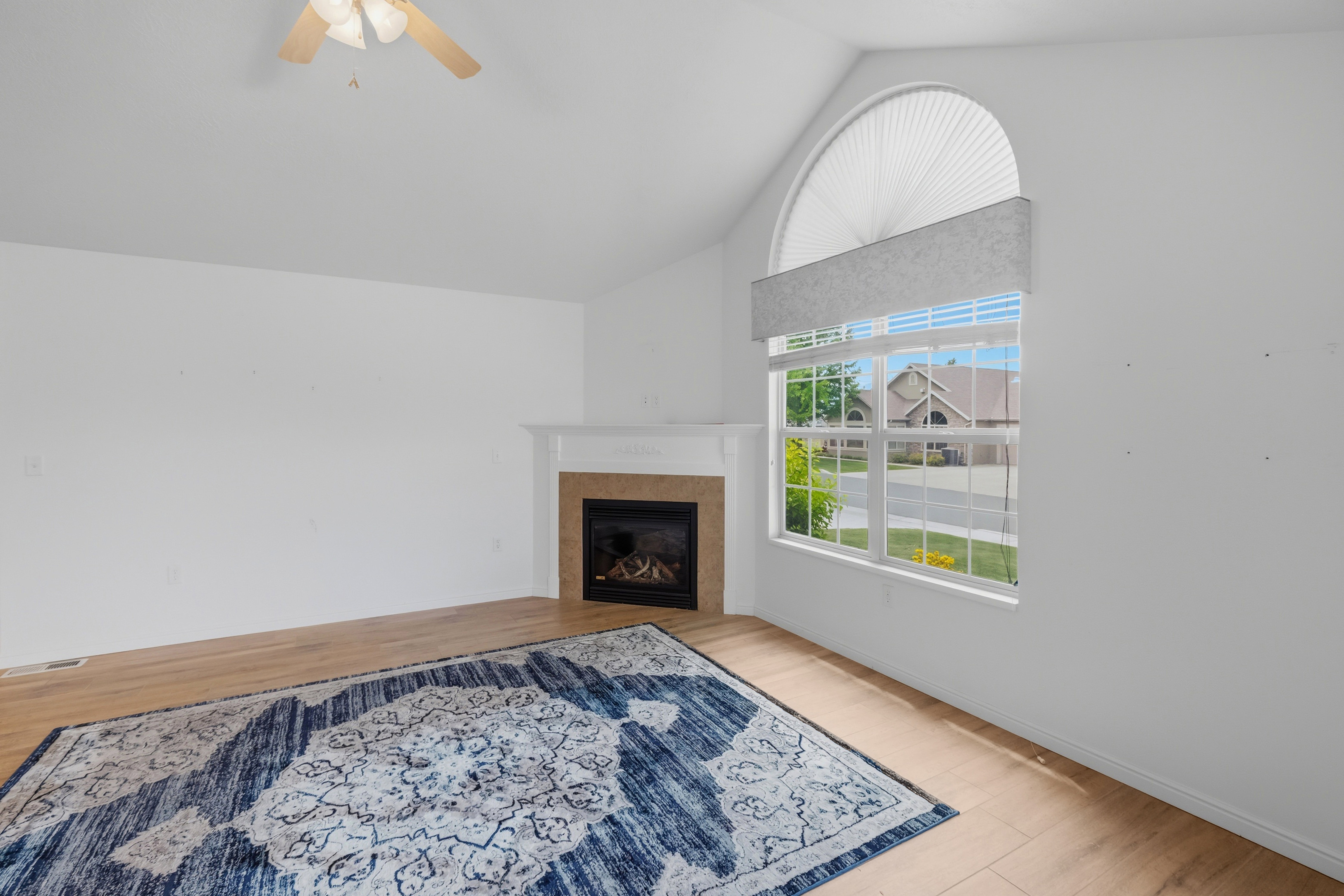 Vaulted ceiling living space featuring a fireplace with a white mantel, a large window with an arched transom, and wood-finish flooring