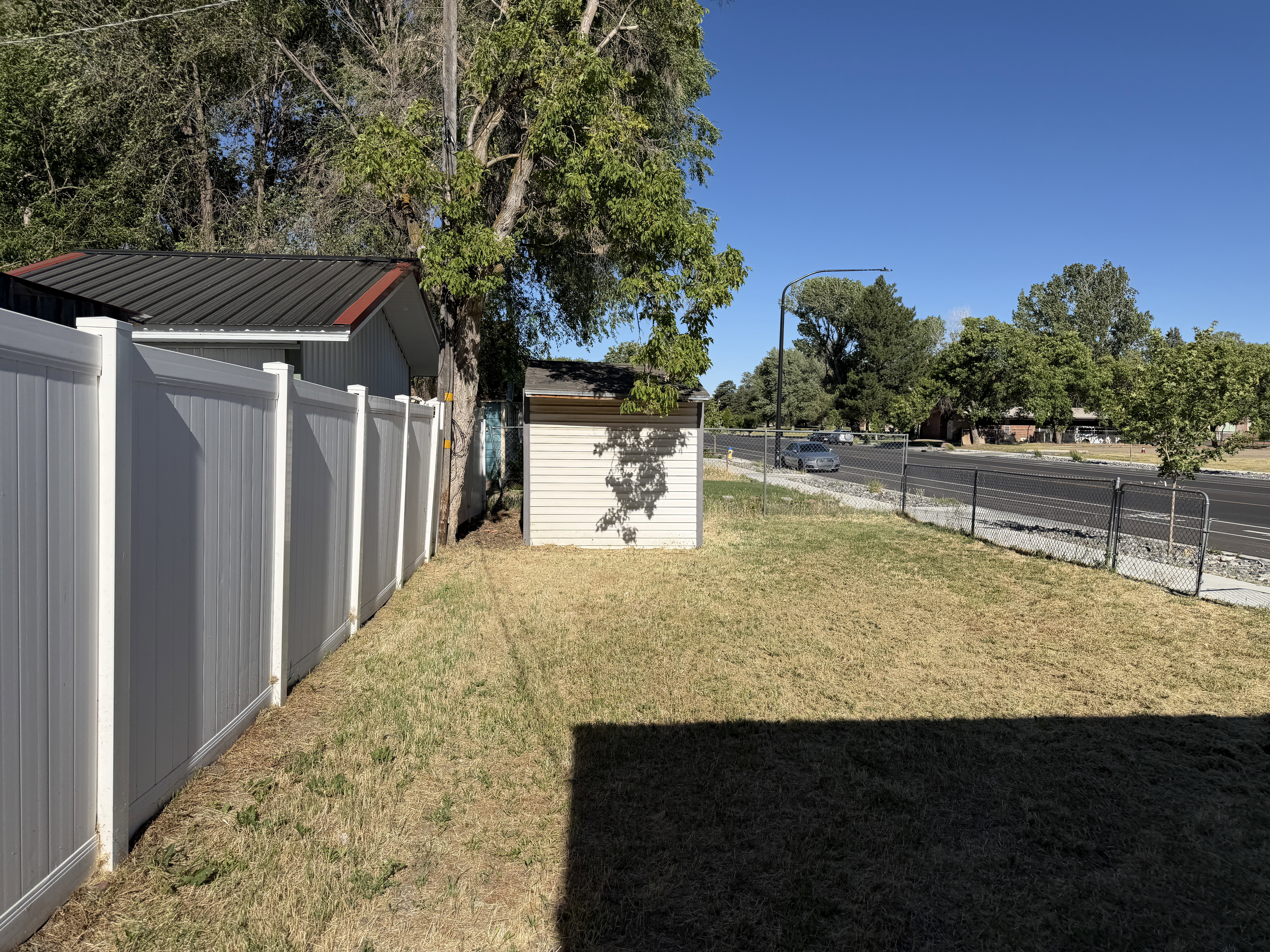 Expansive rear yard featuring a white privacy fence, mature trees, and a utility shed with a dark metal roof