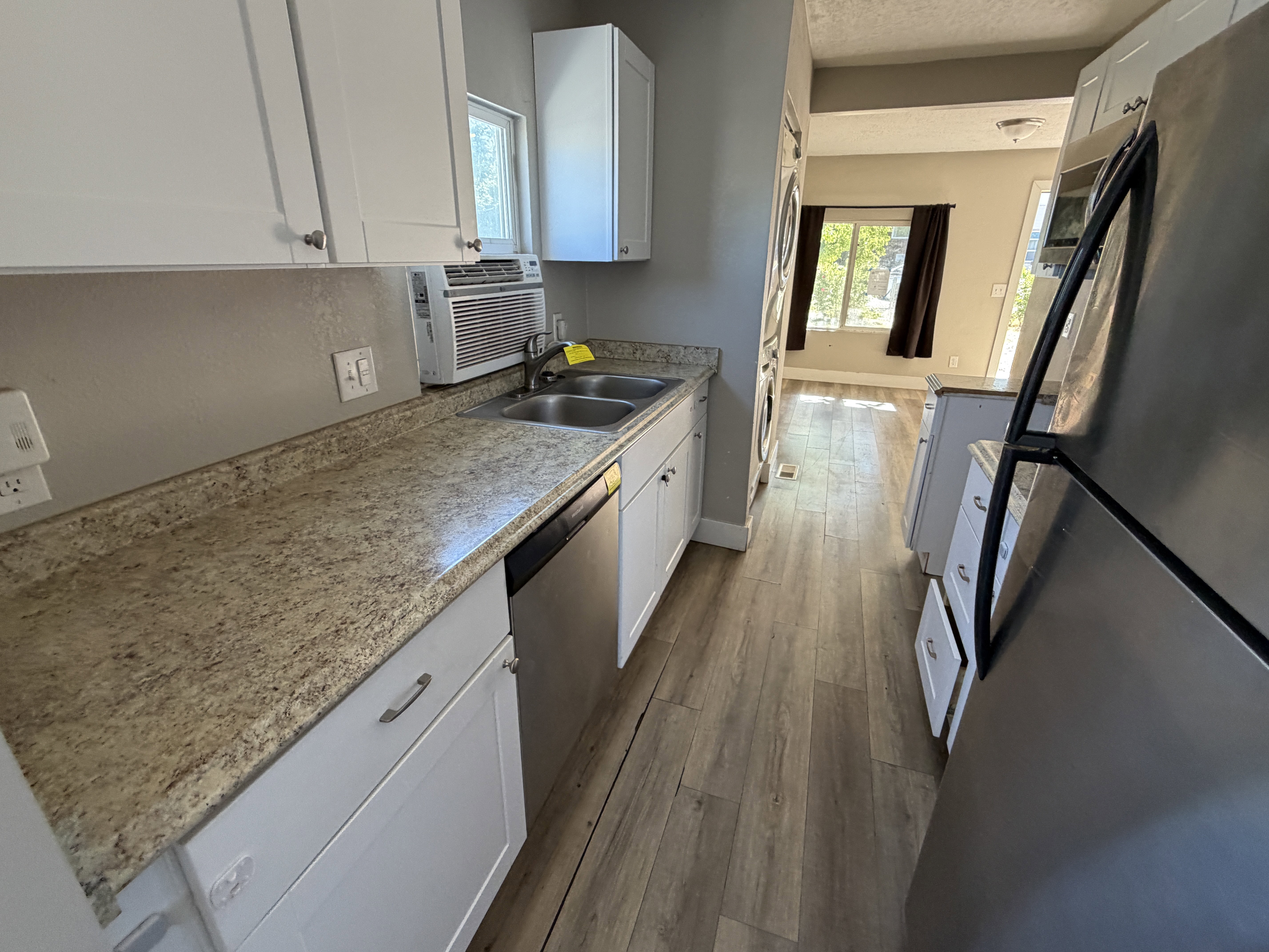 Galley kitchen featuring wood-finish flooring, white cabinetry, a double basin sink, and stainless steel appliances