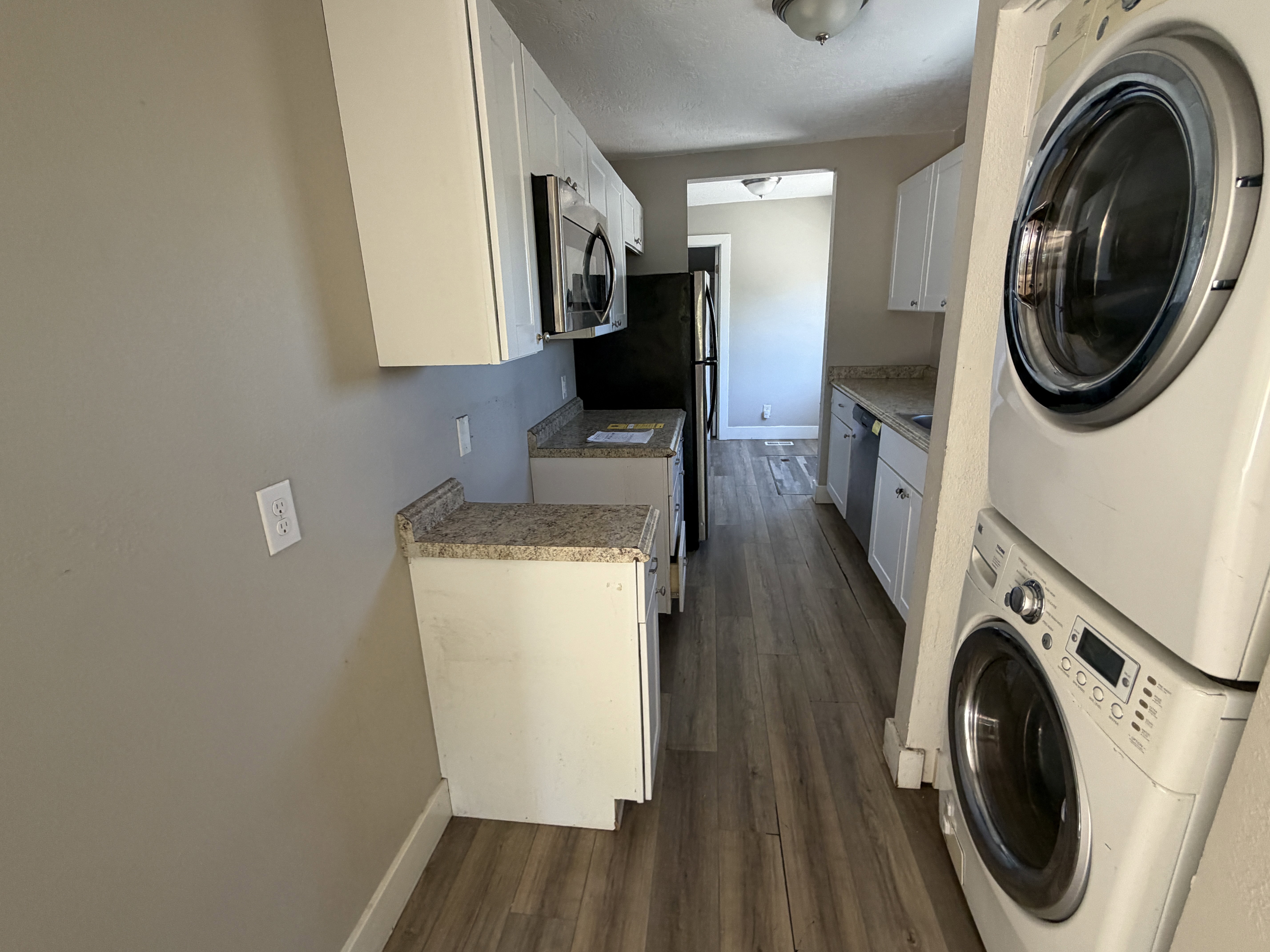 Galley kitchen featuring wood-finish flooring, white cabinetry, granite-look countertops, and stainless steel appliances